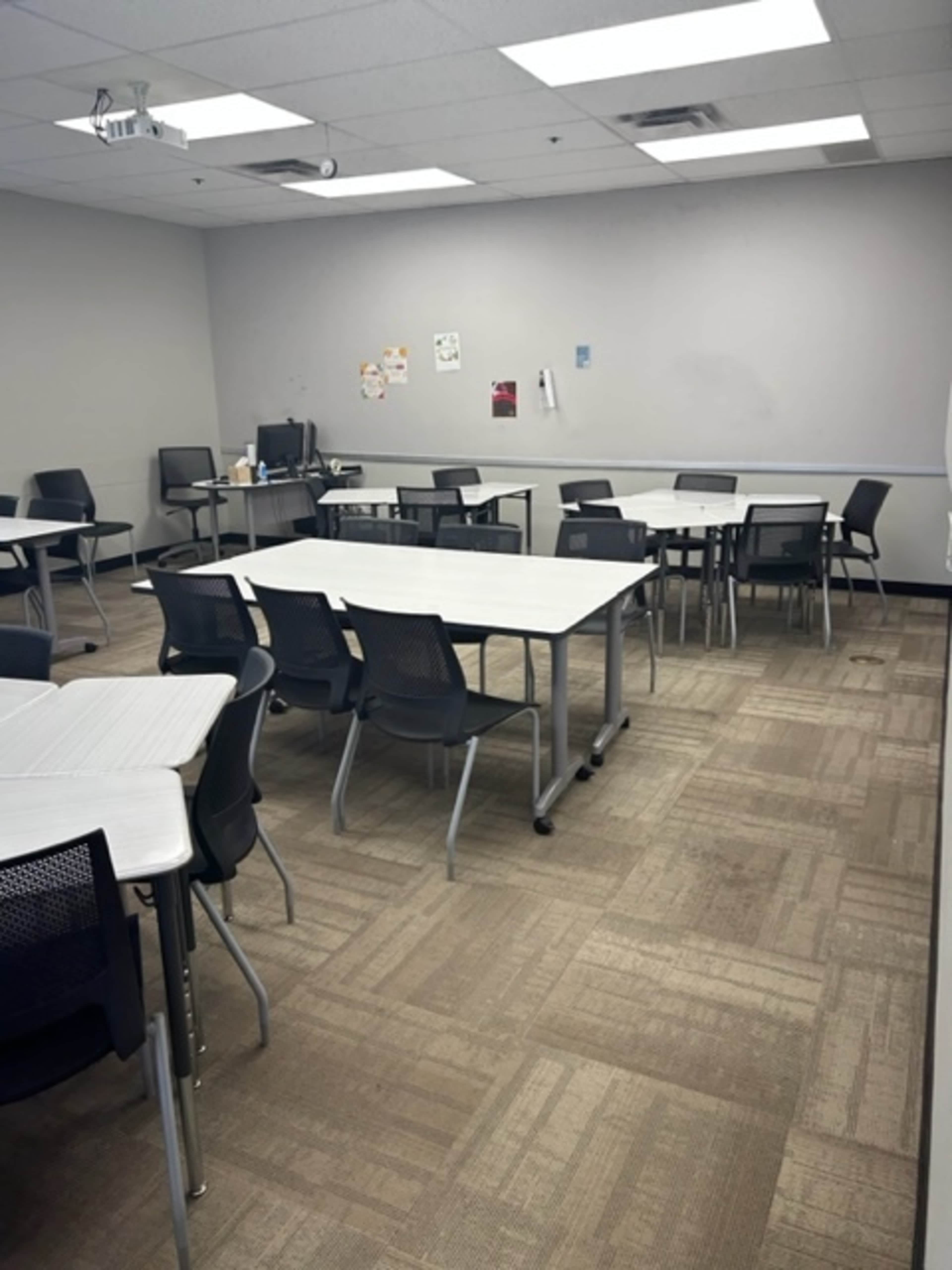 A classroom with several tables and chairs arranged in a mostly empty space.