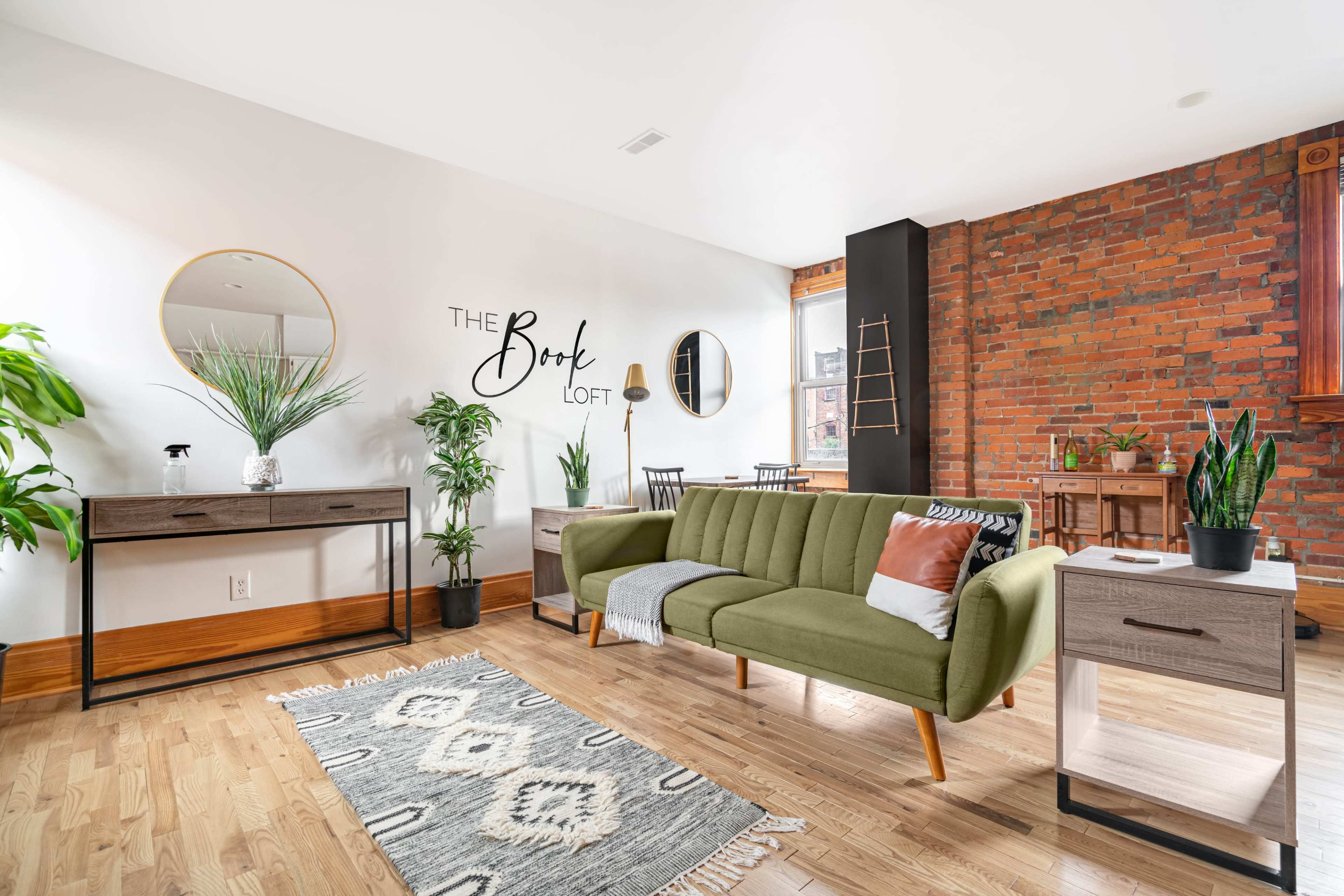 A modern living space featuring a green sofa, wooden furniture, potted plants, and a decorative wall saying "The Book Loft."