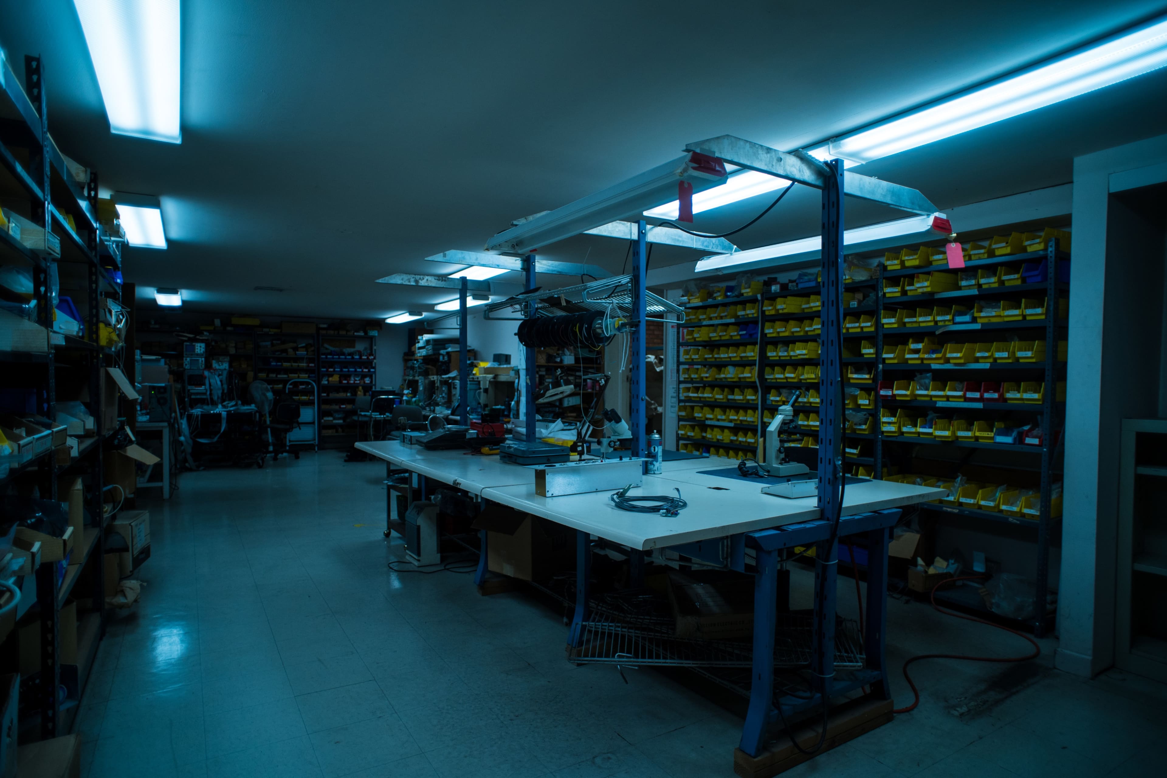 A well-organized workshop with shelves filled with yellow storage bins and a central worktable under fluorescent lighting.