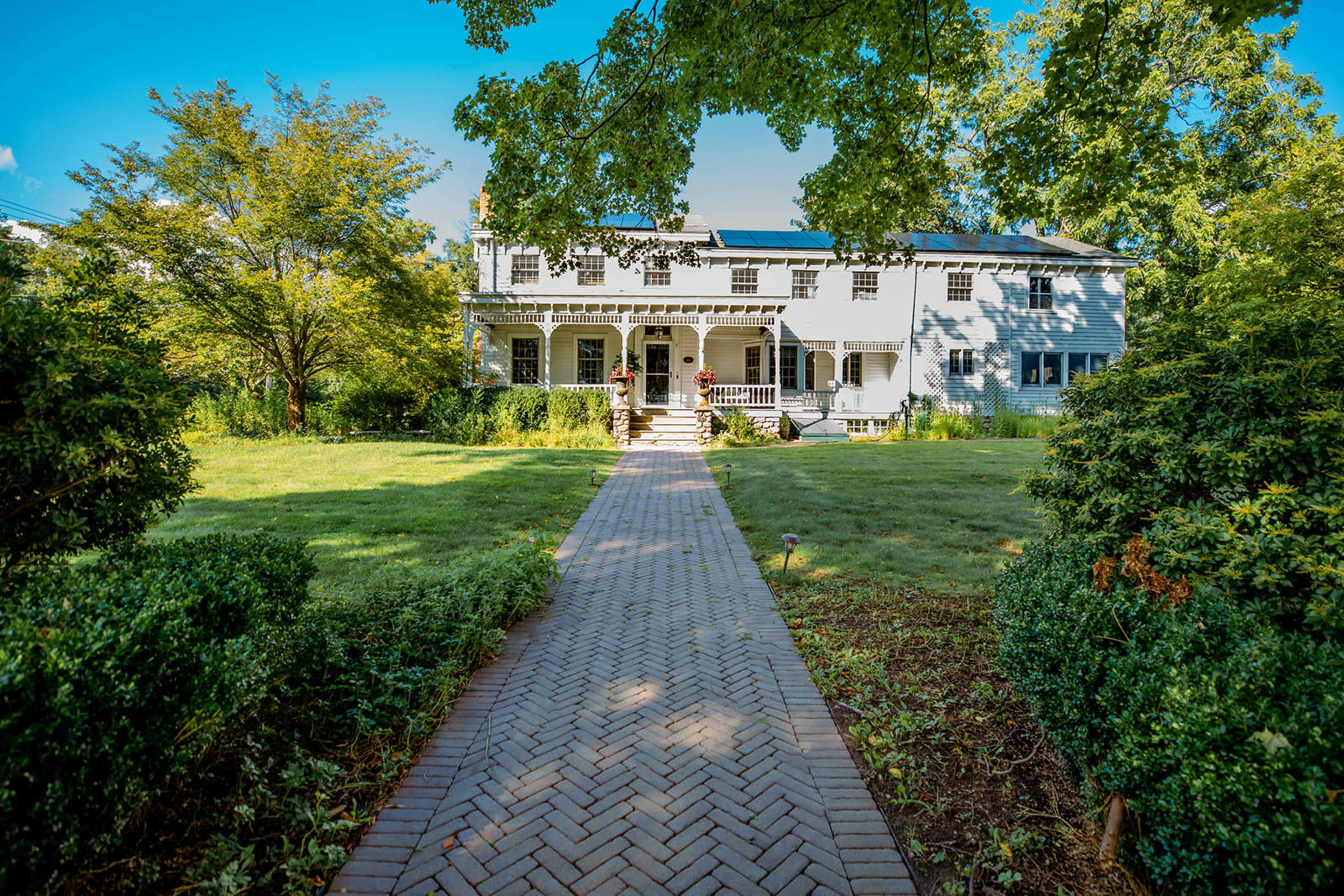 A pathway of brick pavers leads to a two-story house surrounded by greenery.