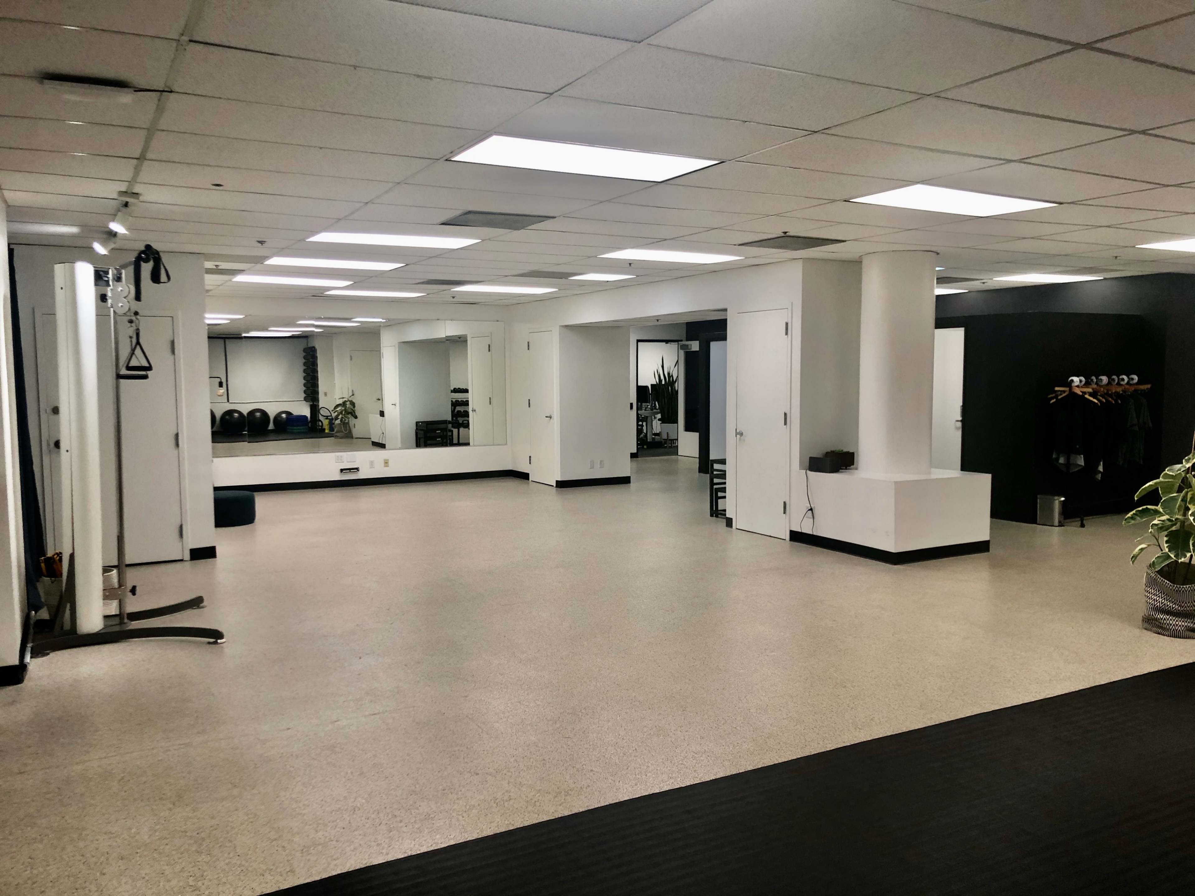 A spacious, well-lit gym or studio with a mirrored wall, exercise equipment, and a minimalist design.