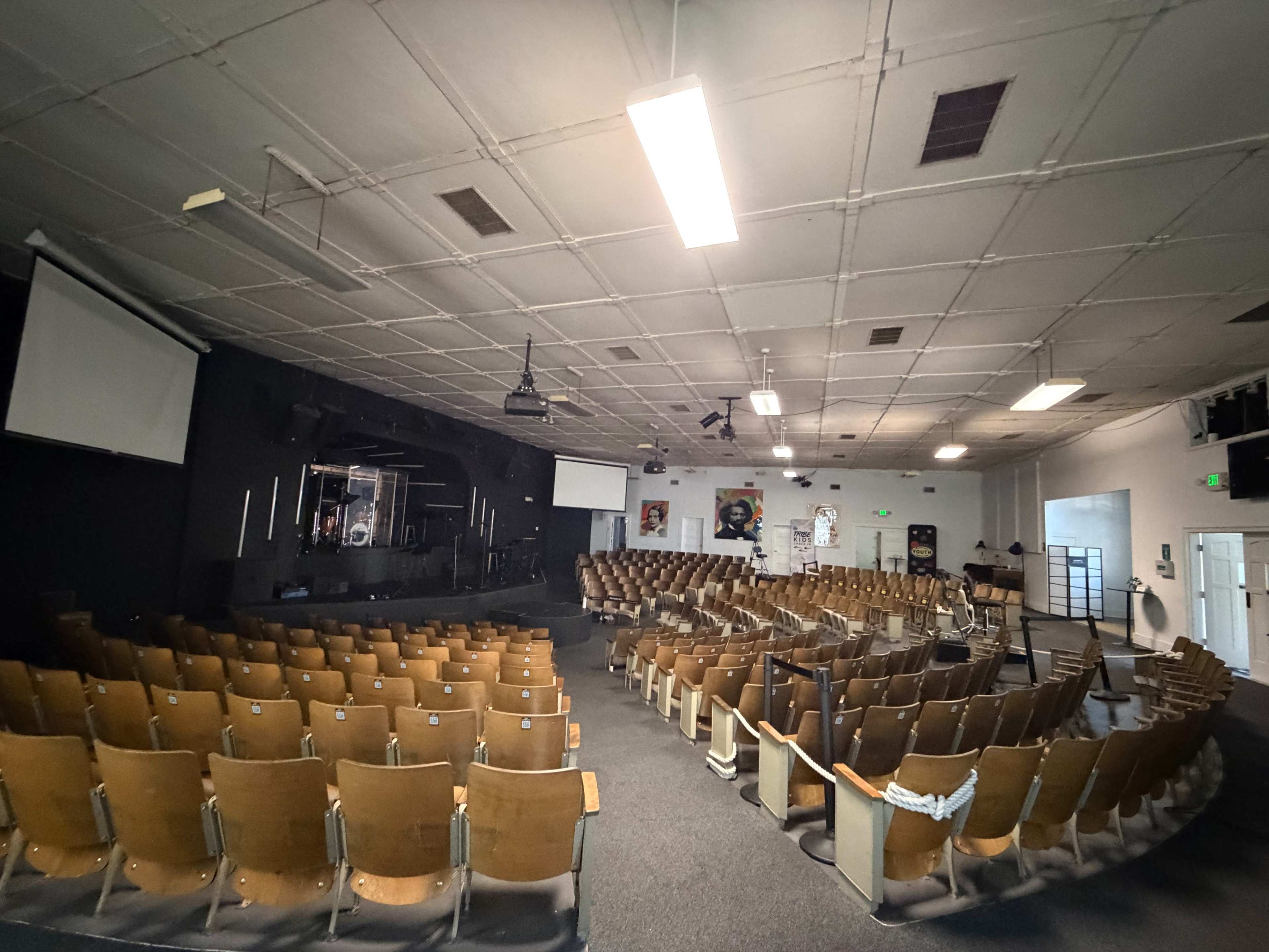 The image shows an empty auditorium with rows of wooden seats facing a raised stage at the front.