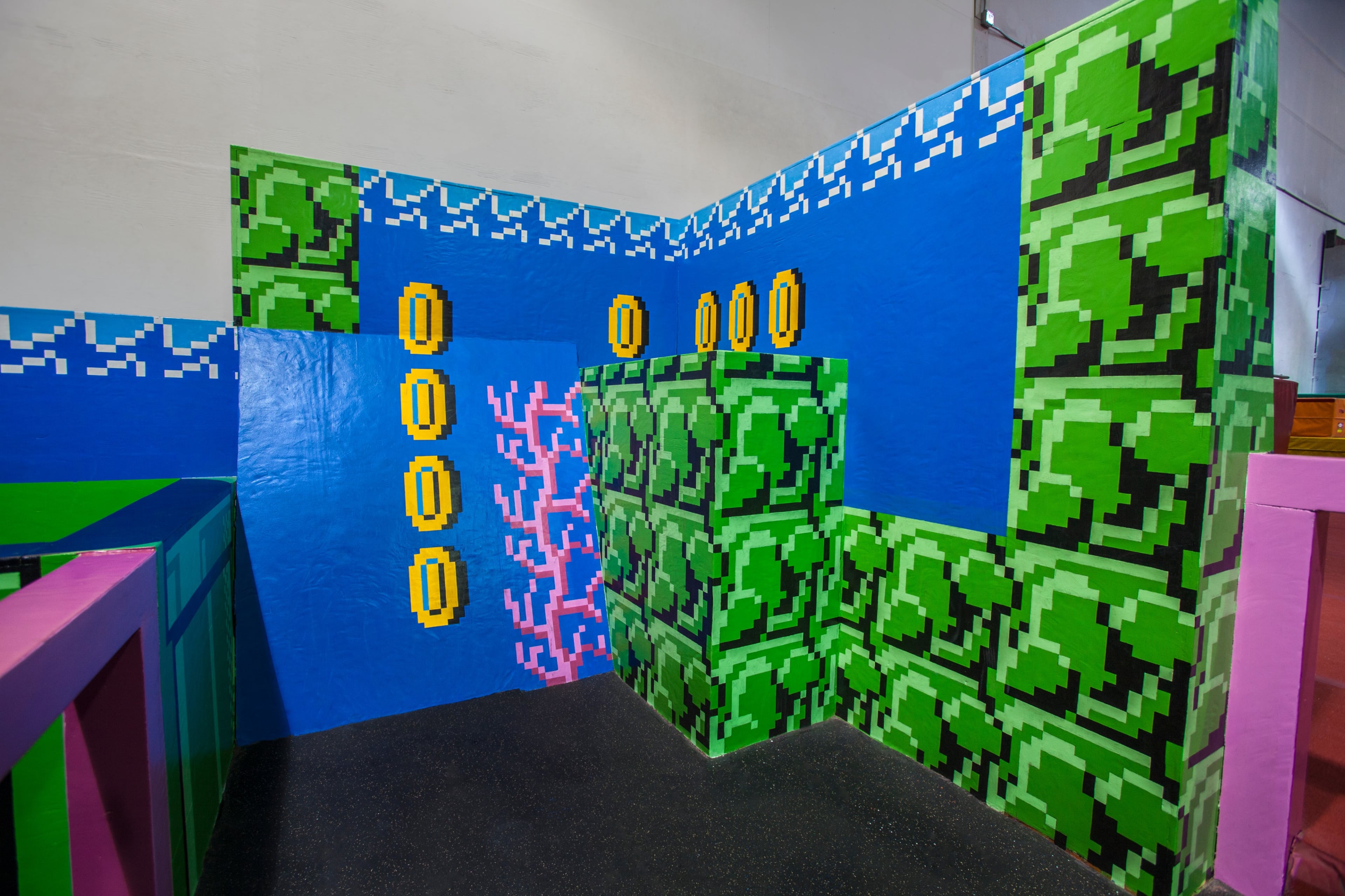 A colorful, pixel-art style wall featuring green brick patterns and yellow coins, reminiscent of classic video game graphics.