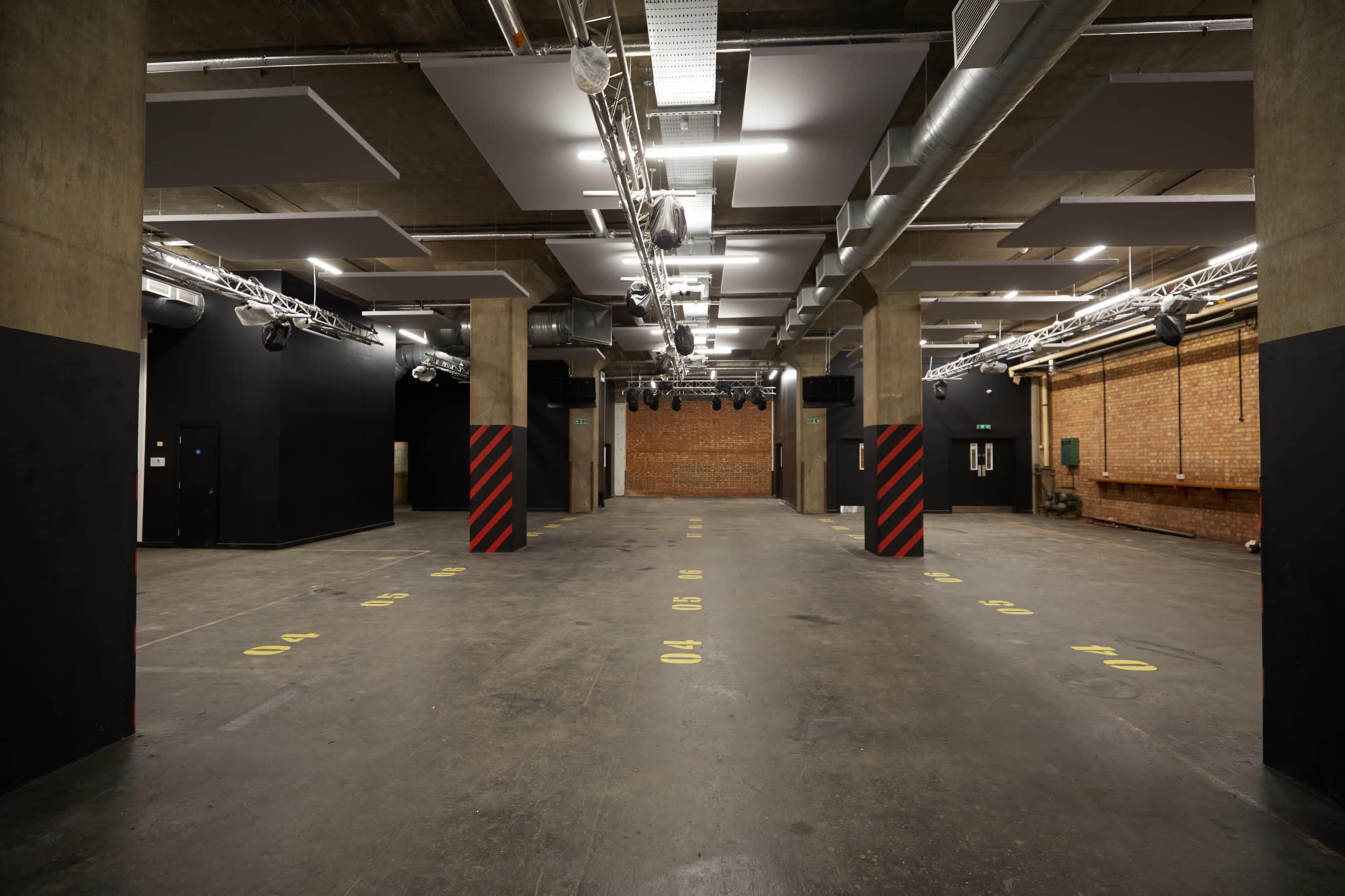 A spacious, industrial-style venue with exposed brick walls, high ceilings, and marked areas on the concrete floor.