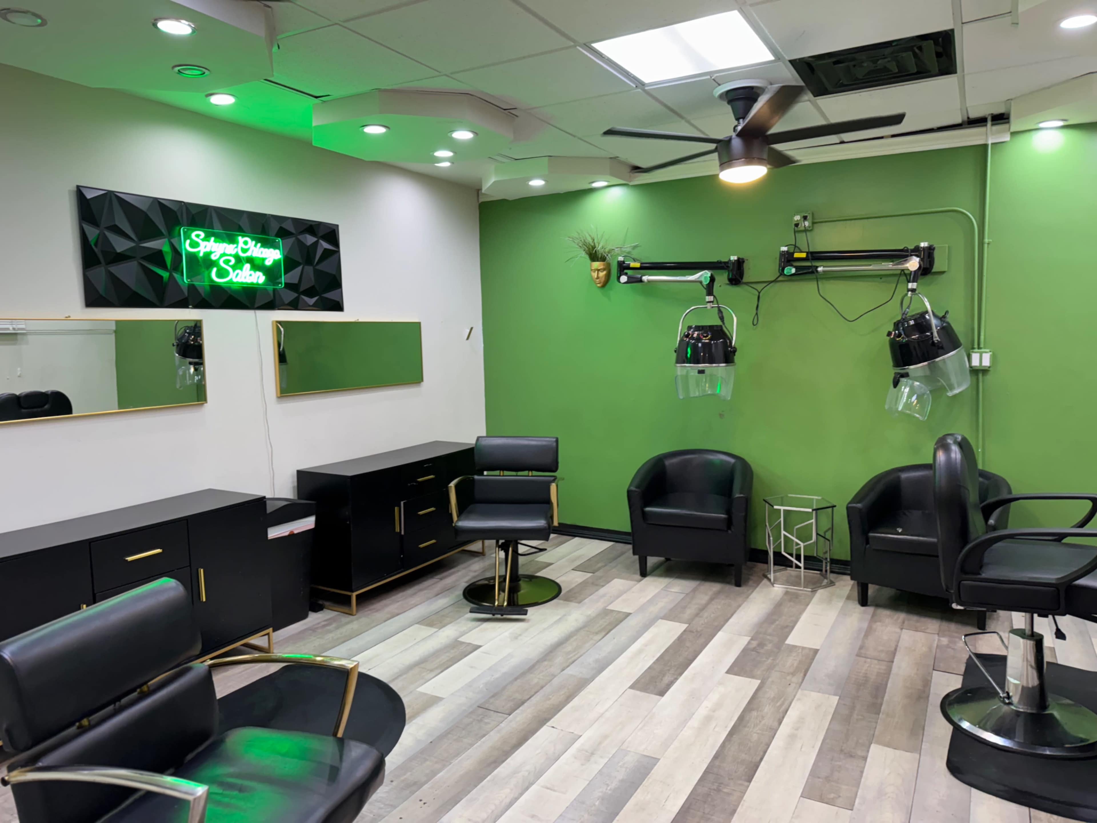 The image shows a modern hair salon interior with black chairs, green walls, and two hairdryers attached to the wall.
