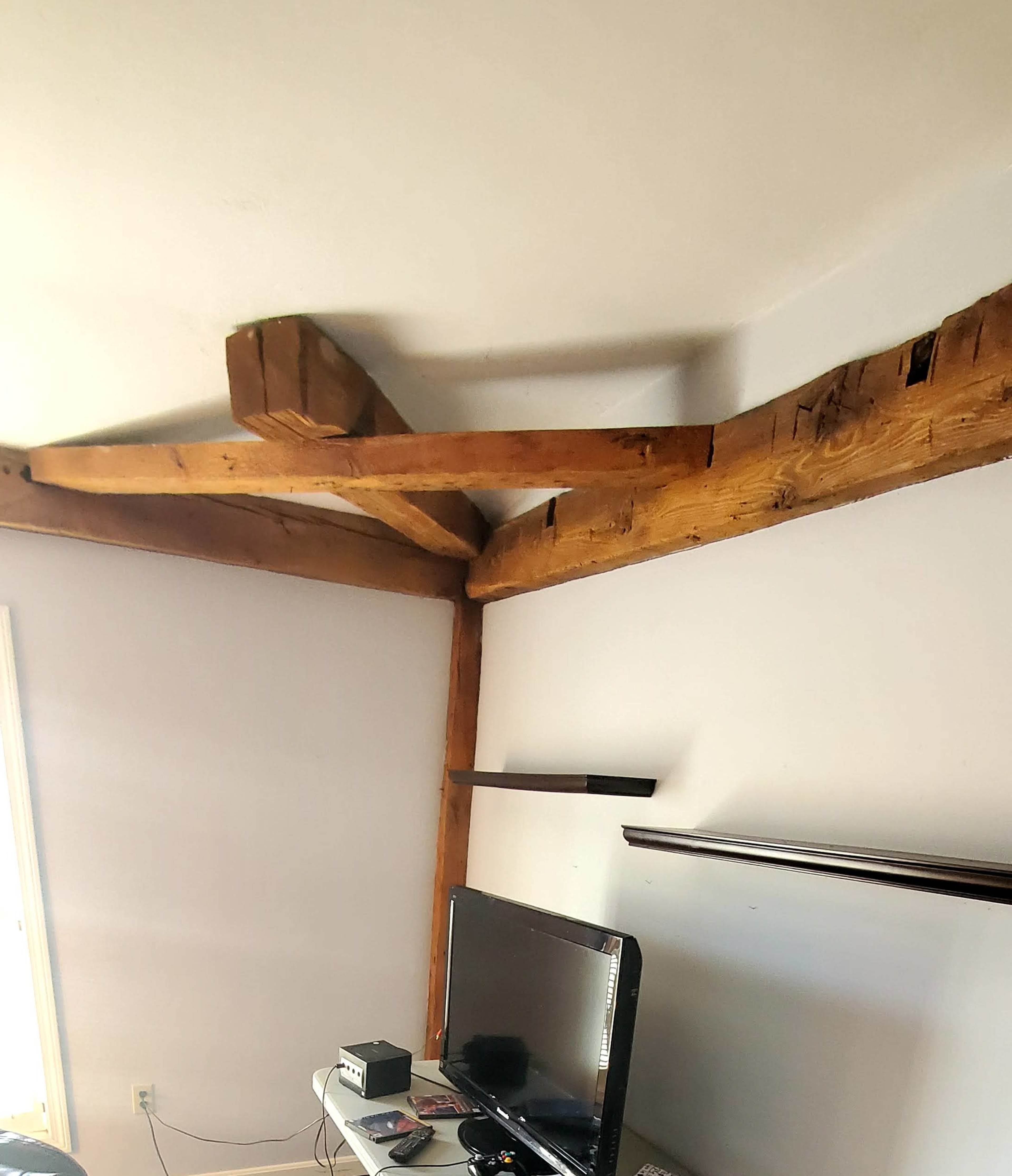A room with wooden ceiling beams and a television on a white shelf against the wall.