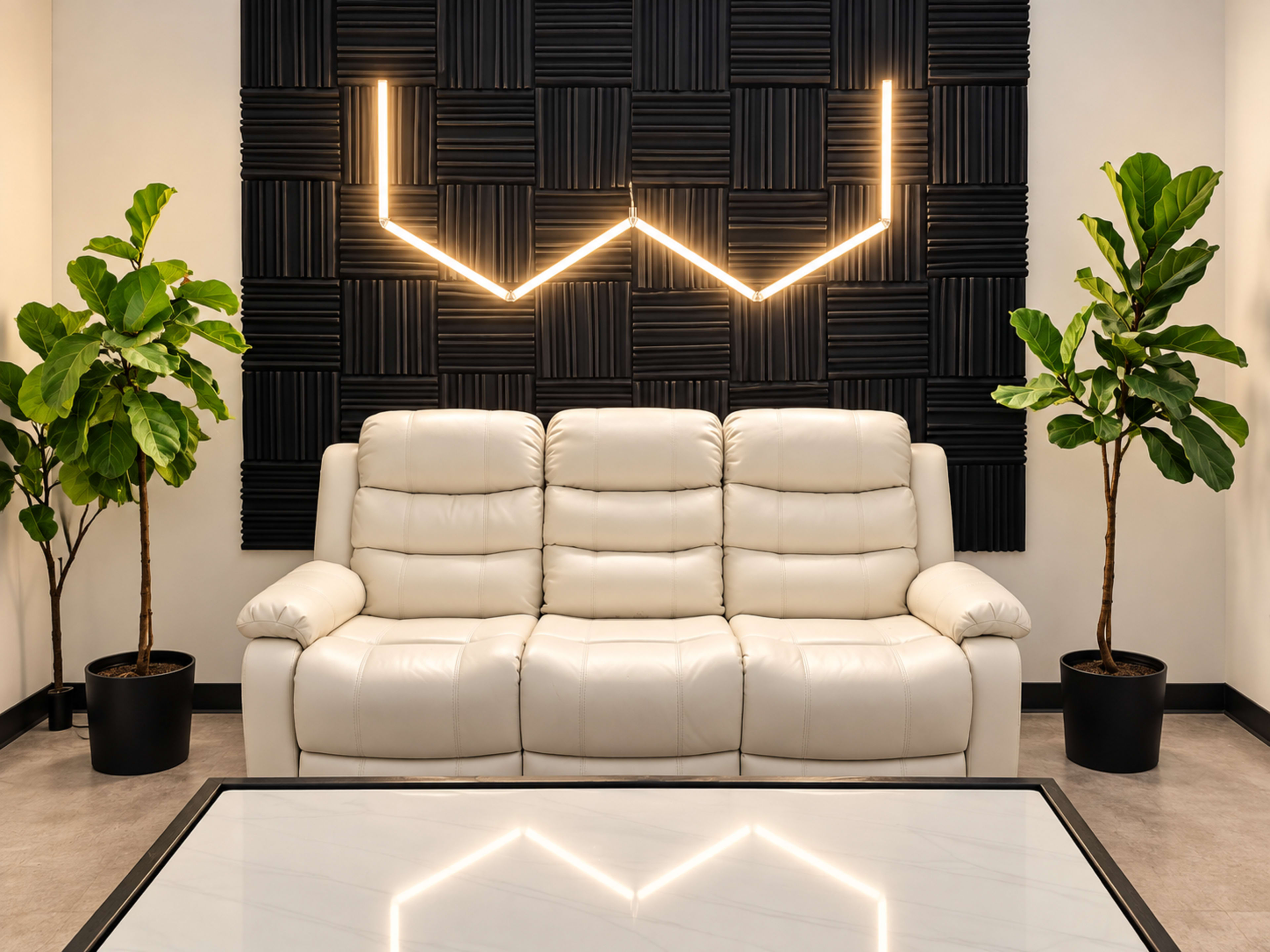 A white leather sofa sits in front of a black textured wall with geometric light fixtures, flanked by potted plants.