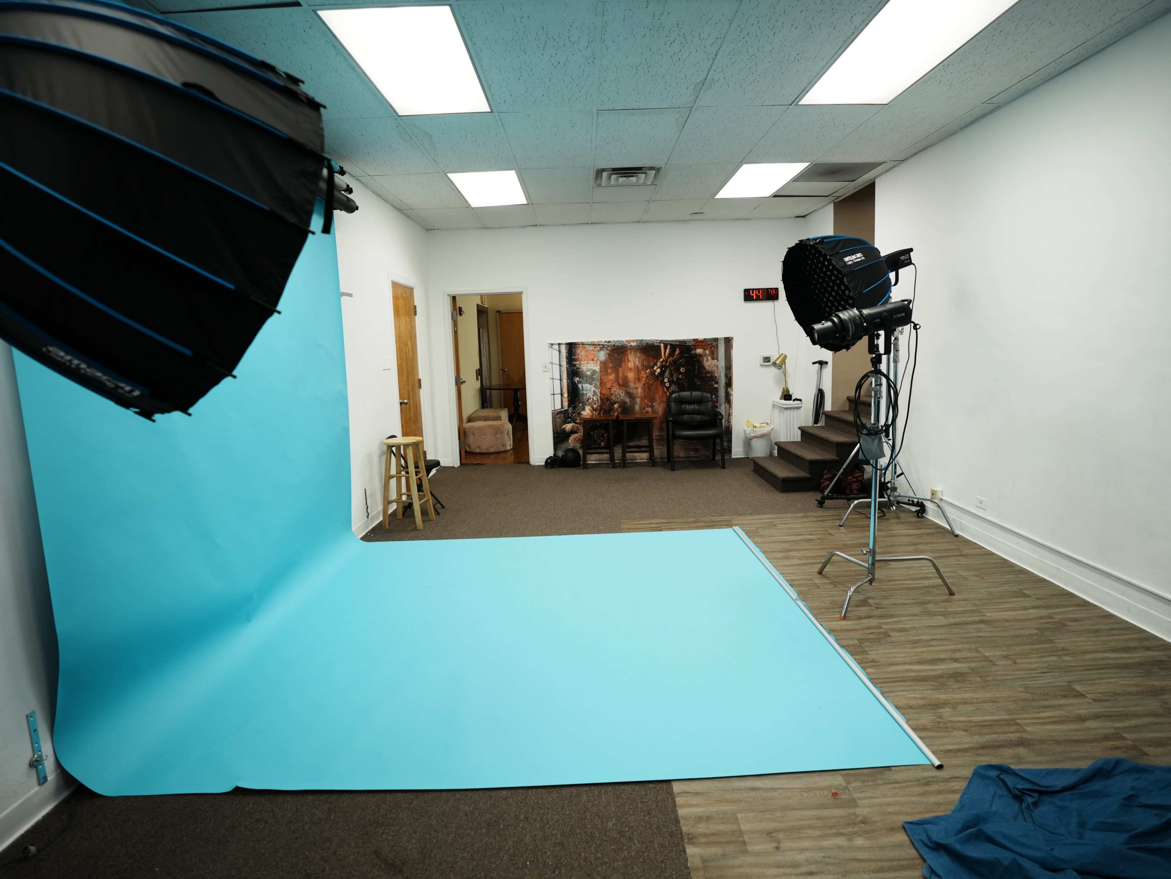 The image shows a photography studio equipped with a blue backdrop, lighting equipment, and a seating area in the background.