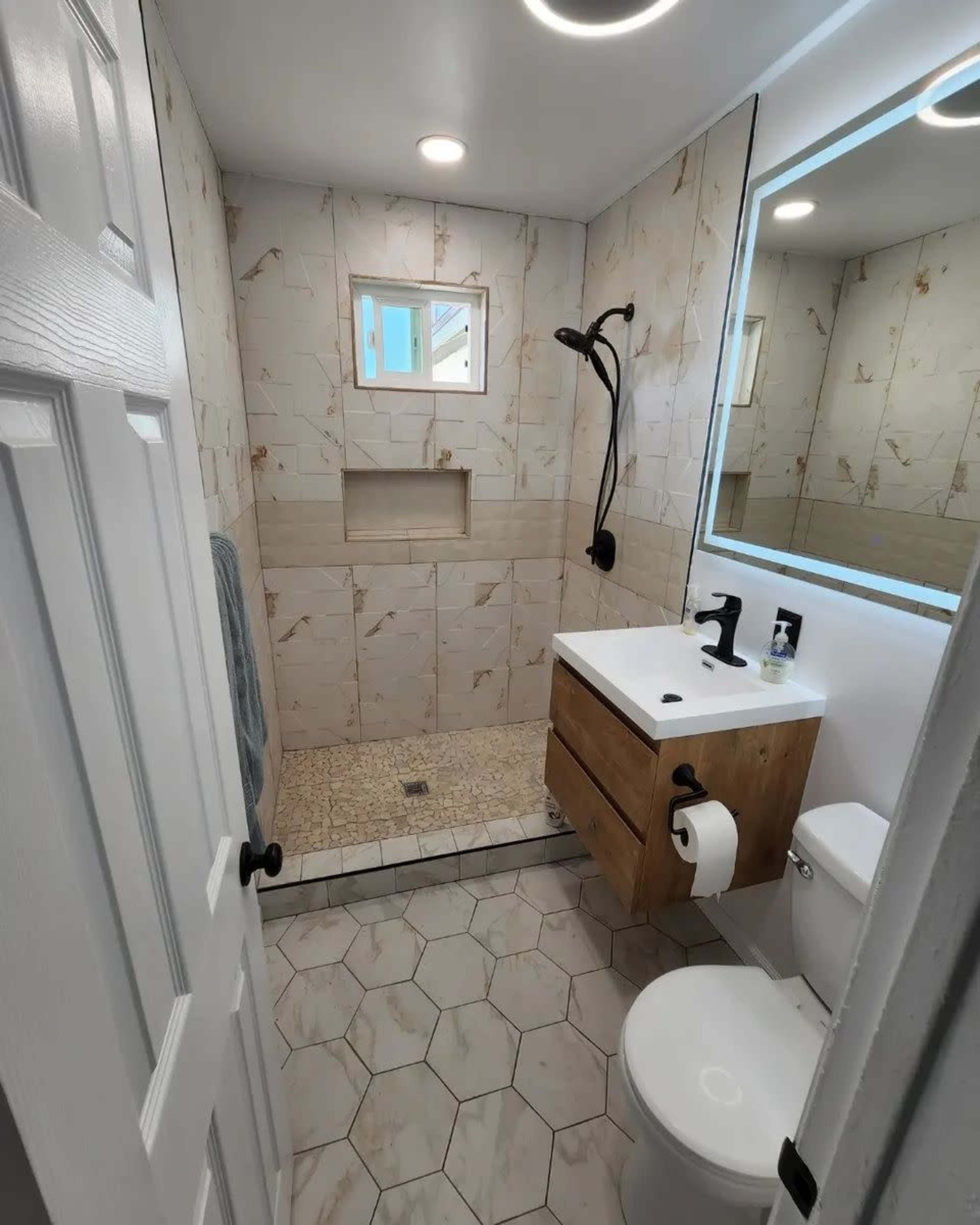 A modern bathroom featuring a walk-in shower with a glass panel, a wooden vanity with a mirror, and hexagonal tiled flooring.