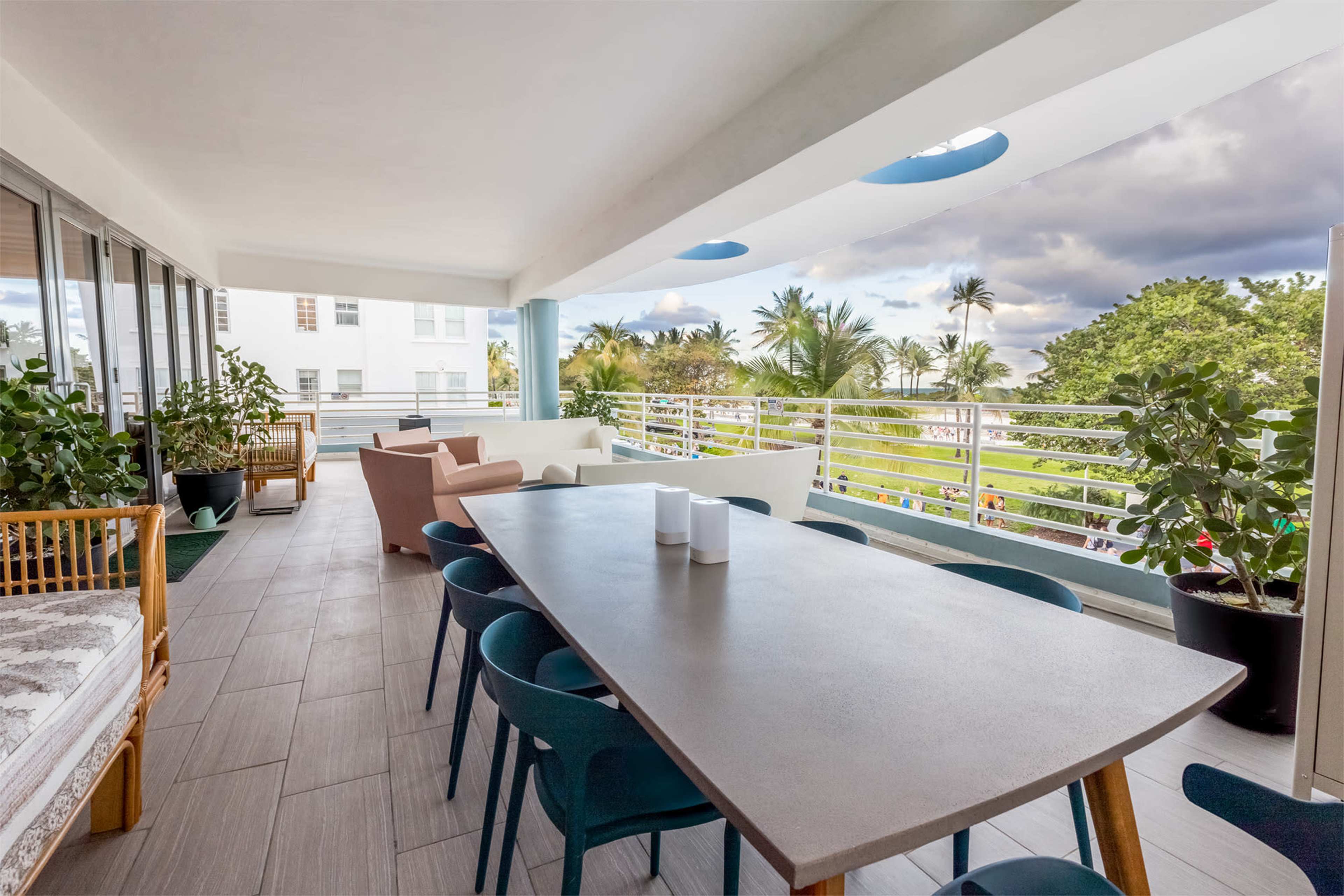A spacious balcony with a long dining table surrounded by chairs, potted plants, and seating areas overlooking a lush landscape.