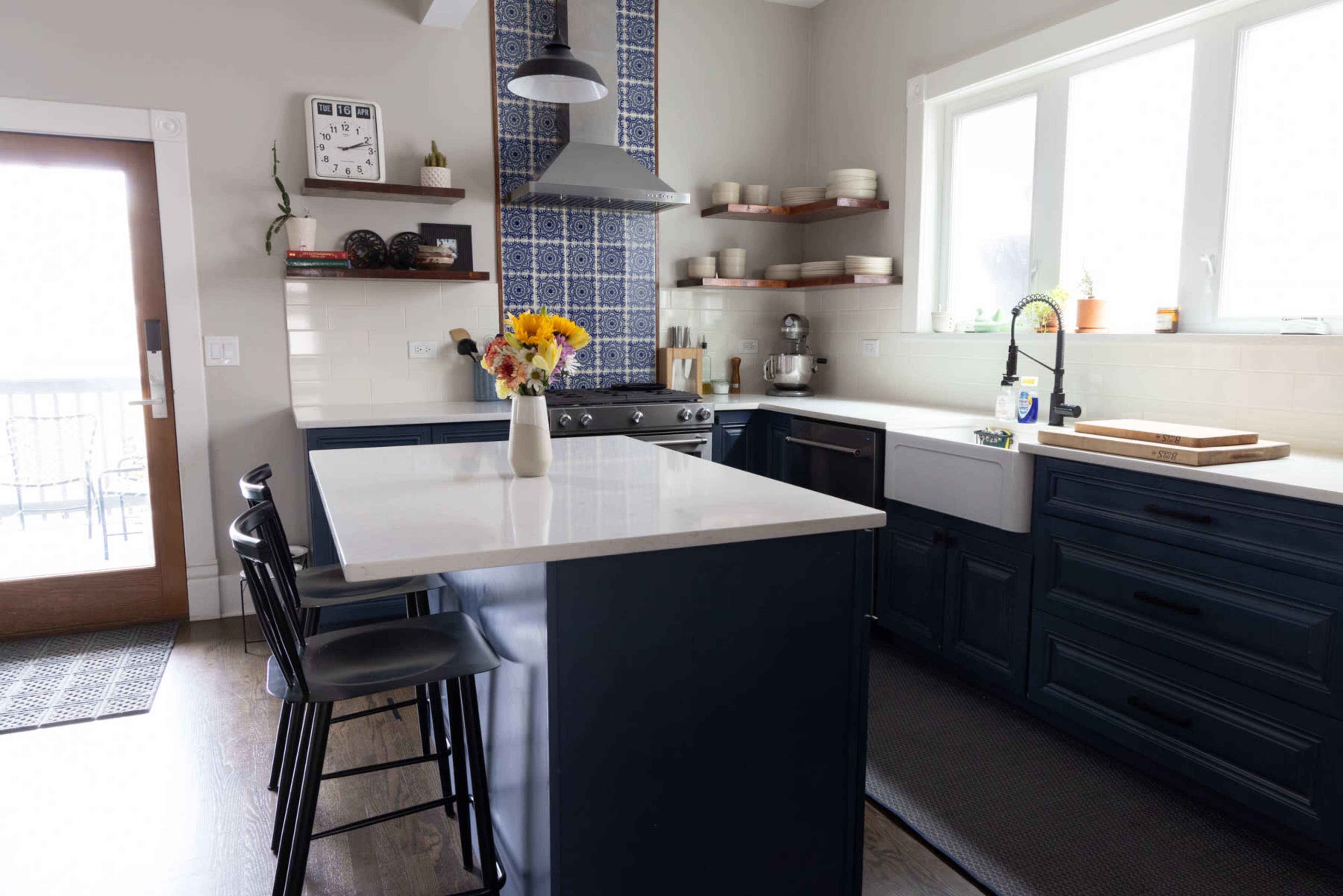 A modern kitchen features a blue cabinetry, a large white countertop island, and decorative wall tiles above the stove.