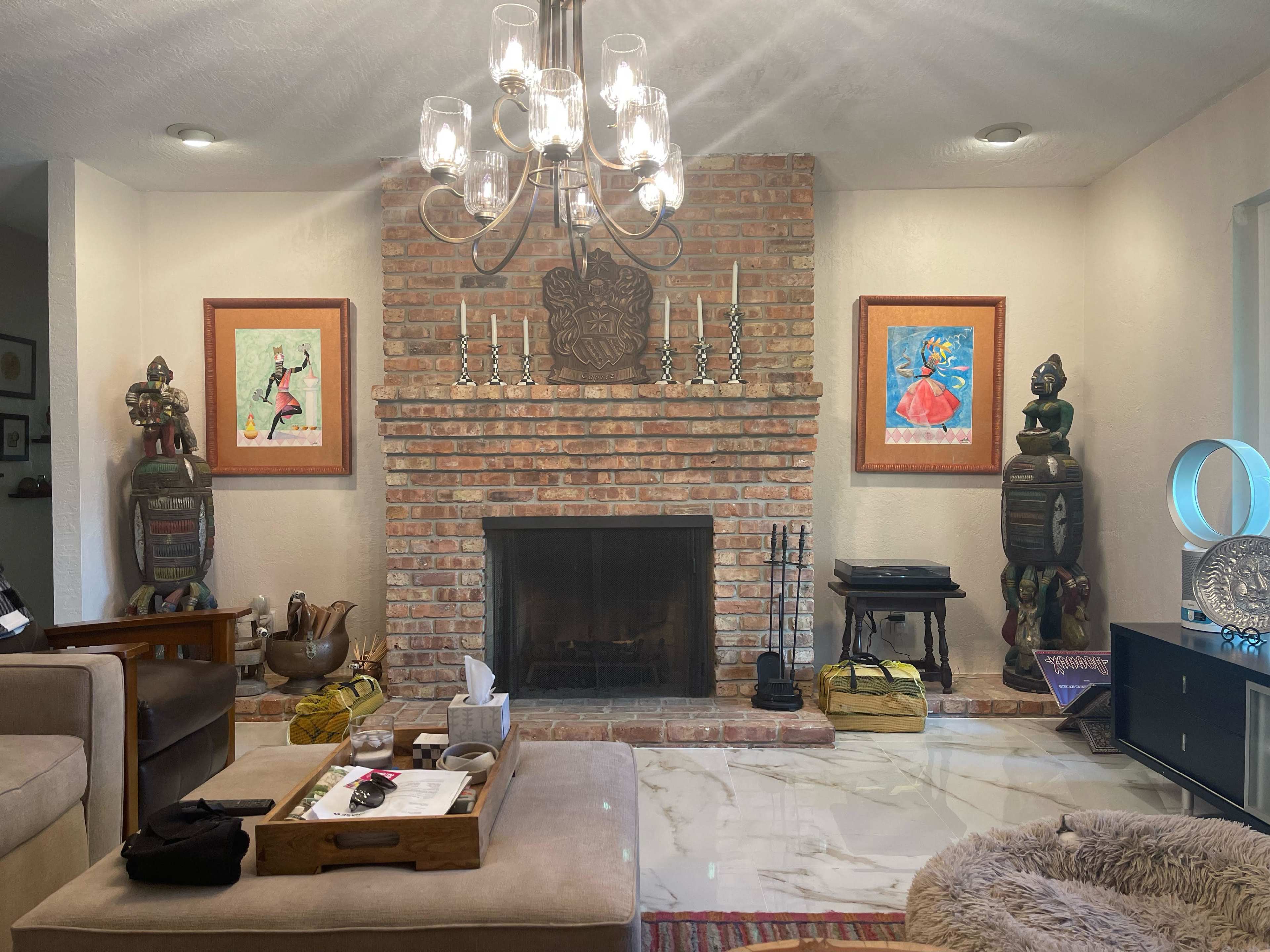 The image shows a living room featuring a brick fireplace, framed artwork on the walls, and decorative sculptures beside the fireplace.