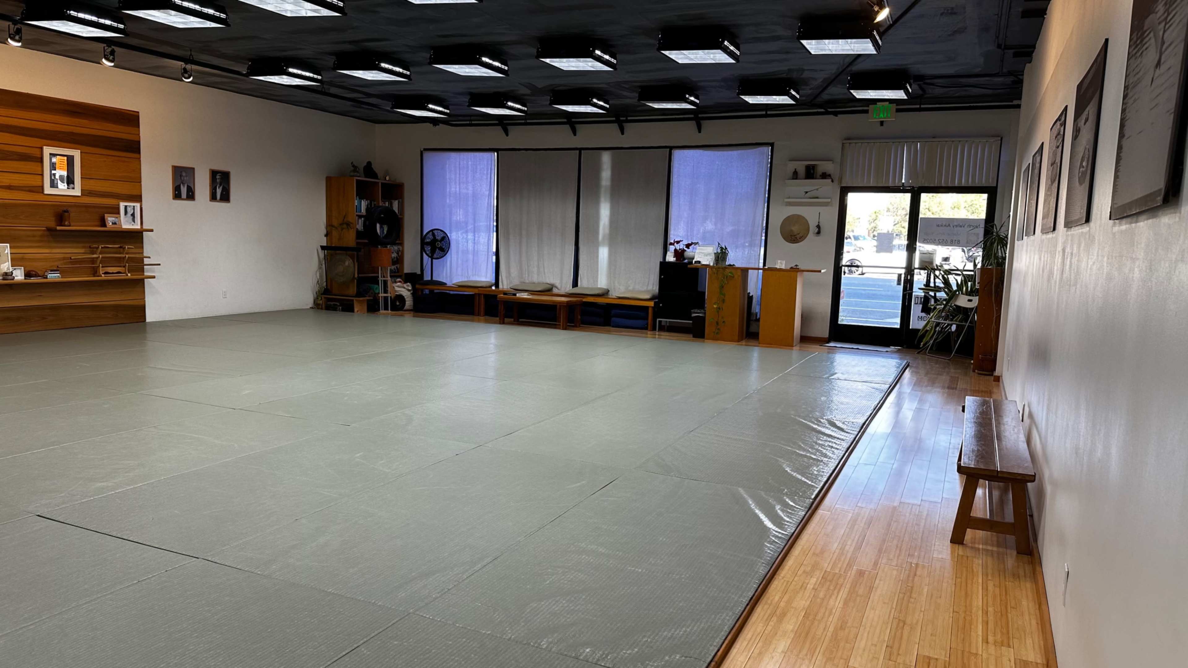 A spacious, empty martial arts studio with tatami mats, wooden benches, and large windows allowing natural light in.