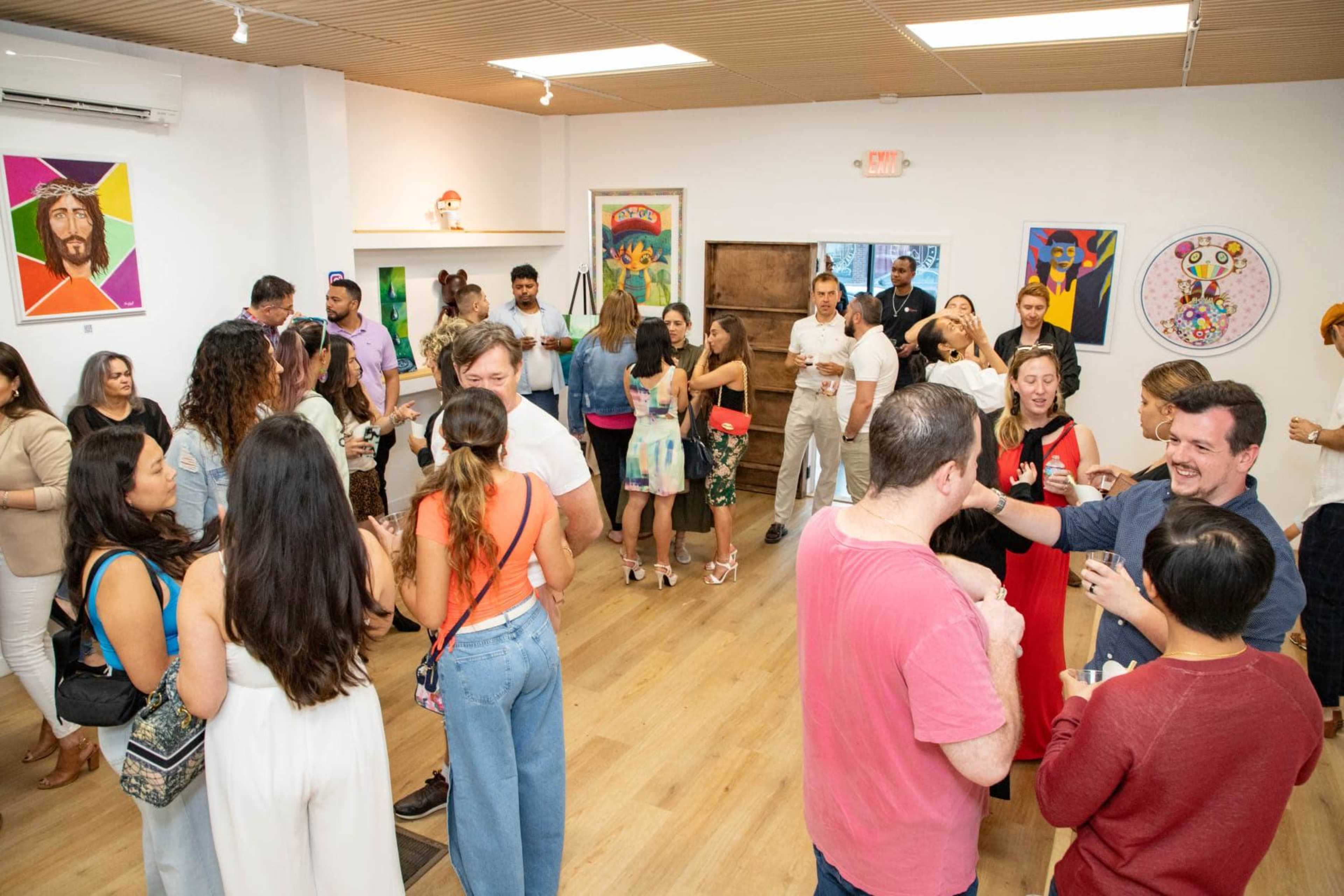 A group of people socialize and enjoy drinks at an event in a brightly lit art gallery.