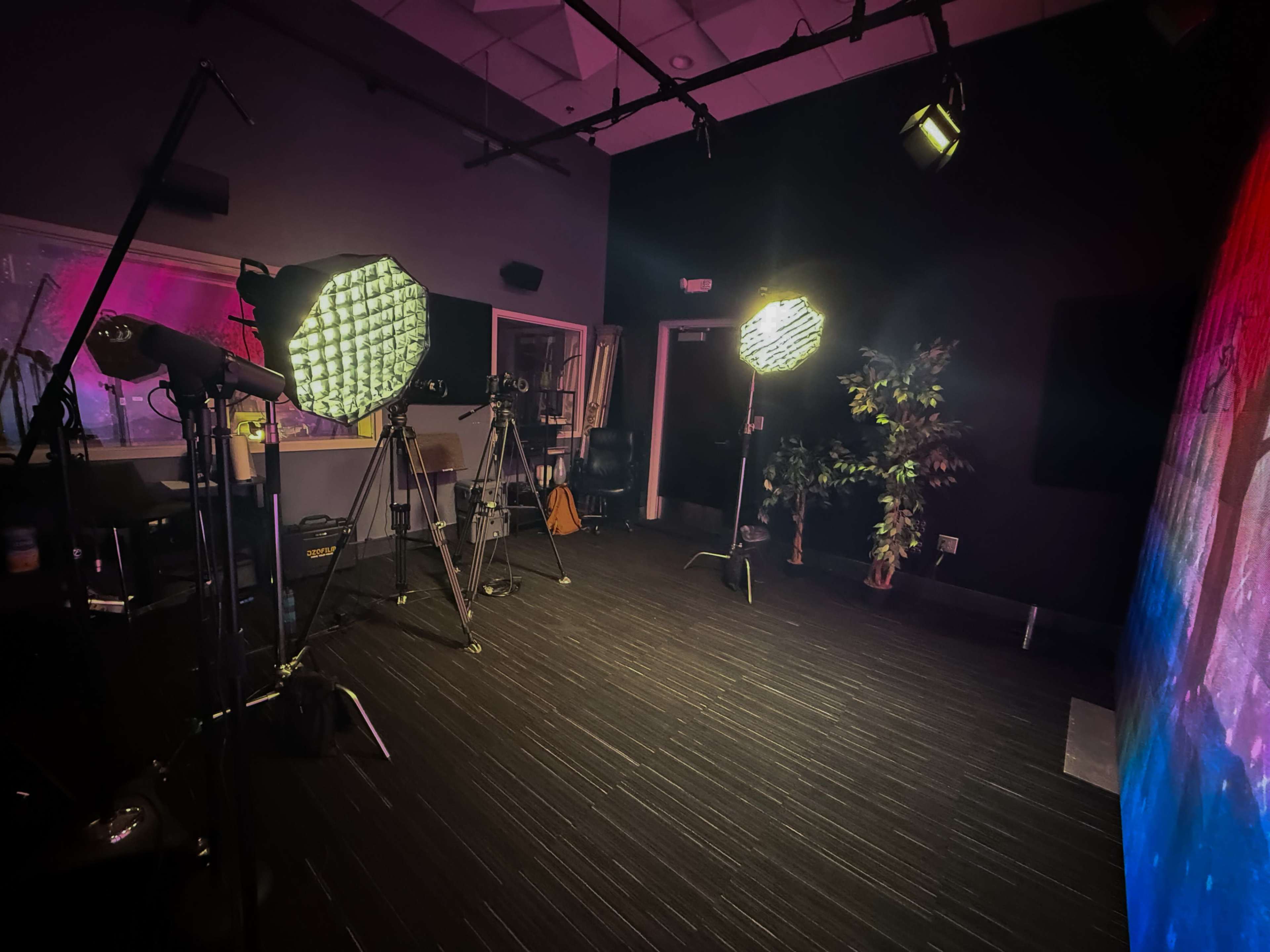 The image depicts a studio setup with several tripods, lighting equipment, and a backdrop.