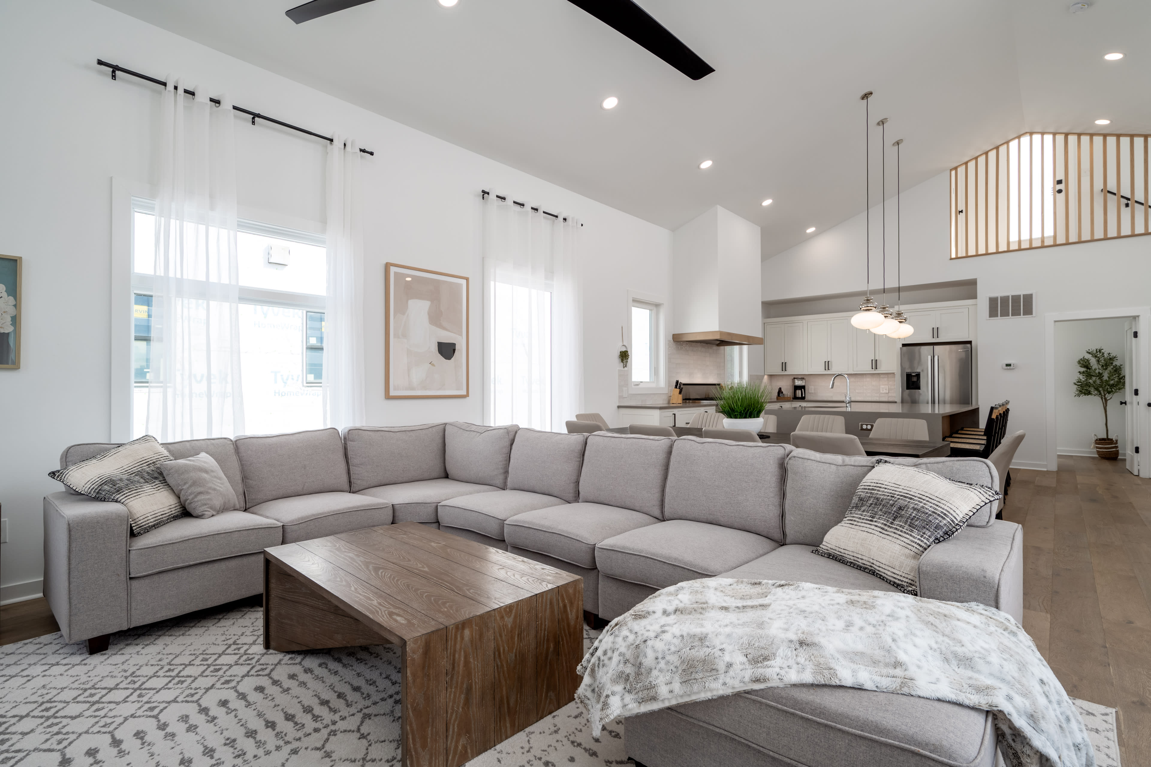 A spacious living room features a large gray sectional sofa, a wooden coffee table, and an open kitchen in the background.
