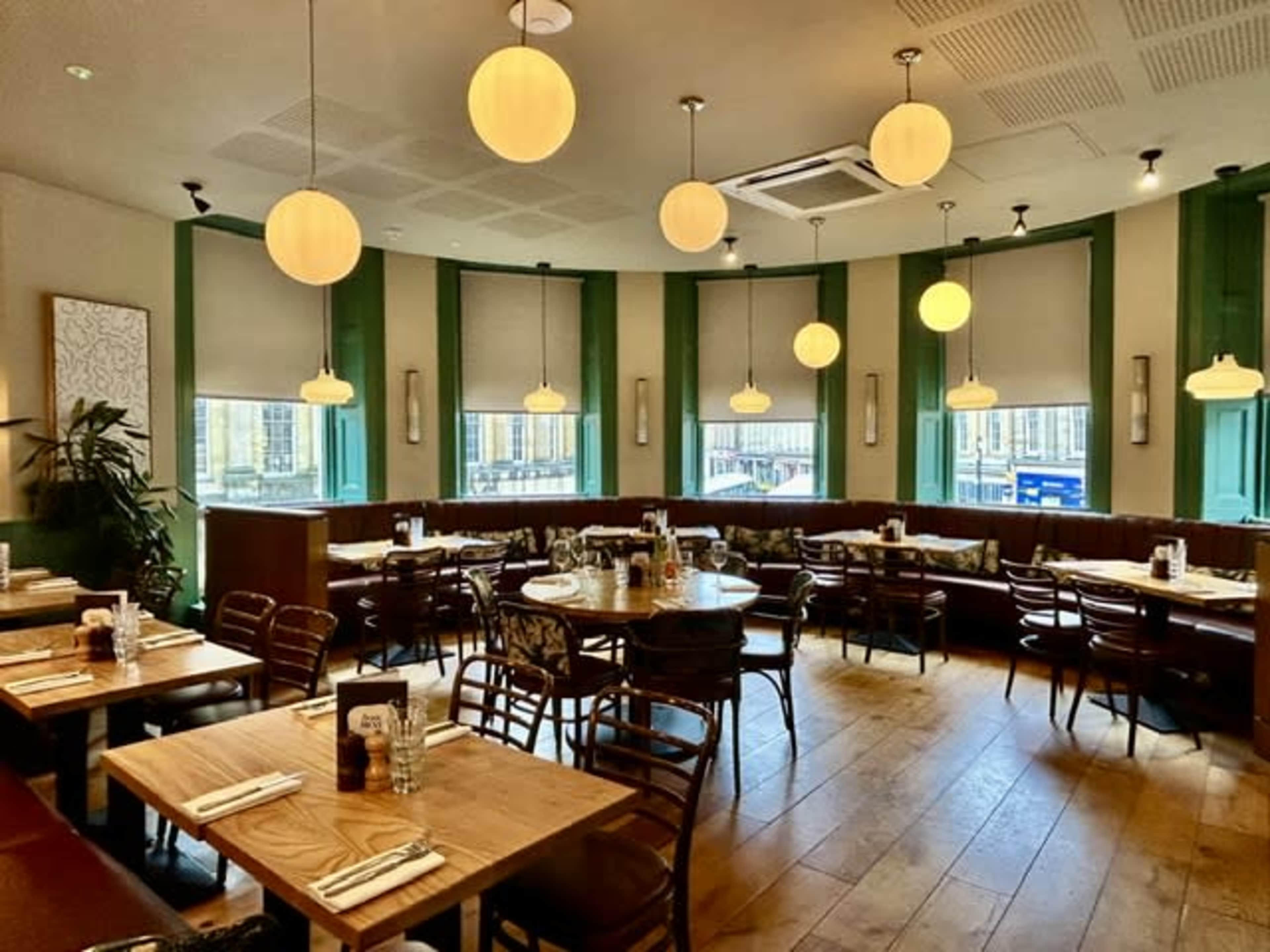 The image shows a modern restaurant with circular pendant lights, wooden tables, and green accent walls.