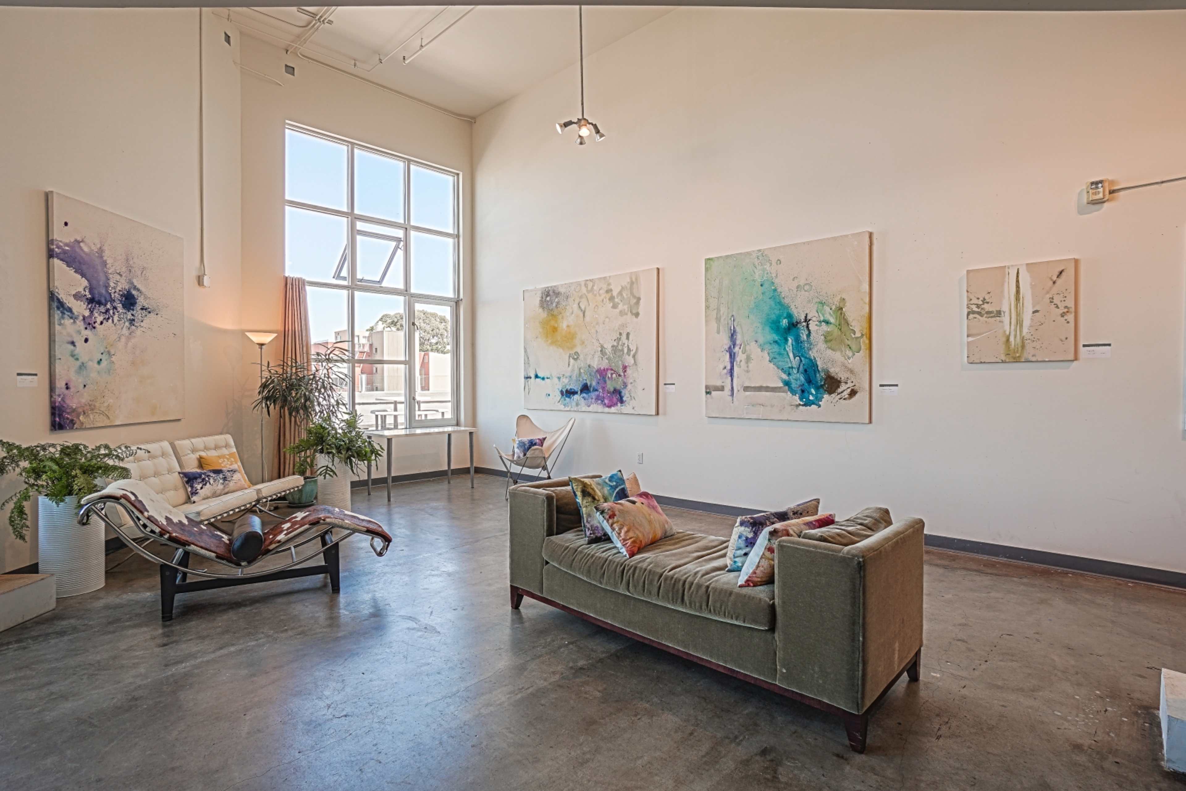 A brightly lit art gallery with modern paintings on the walls and contemporary seating arrangements.