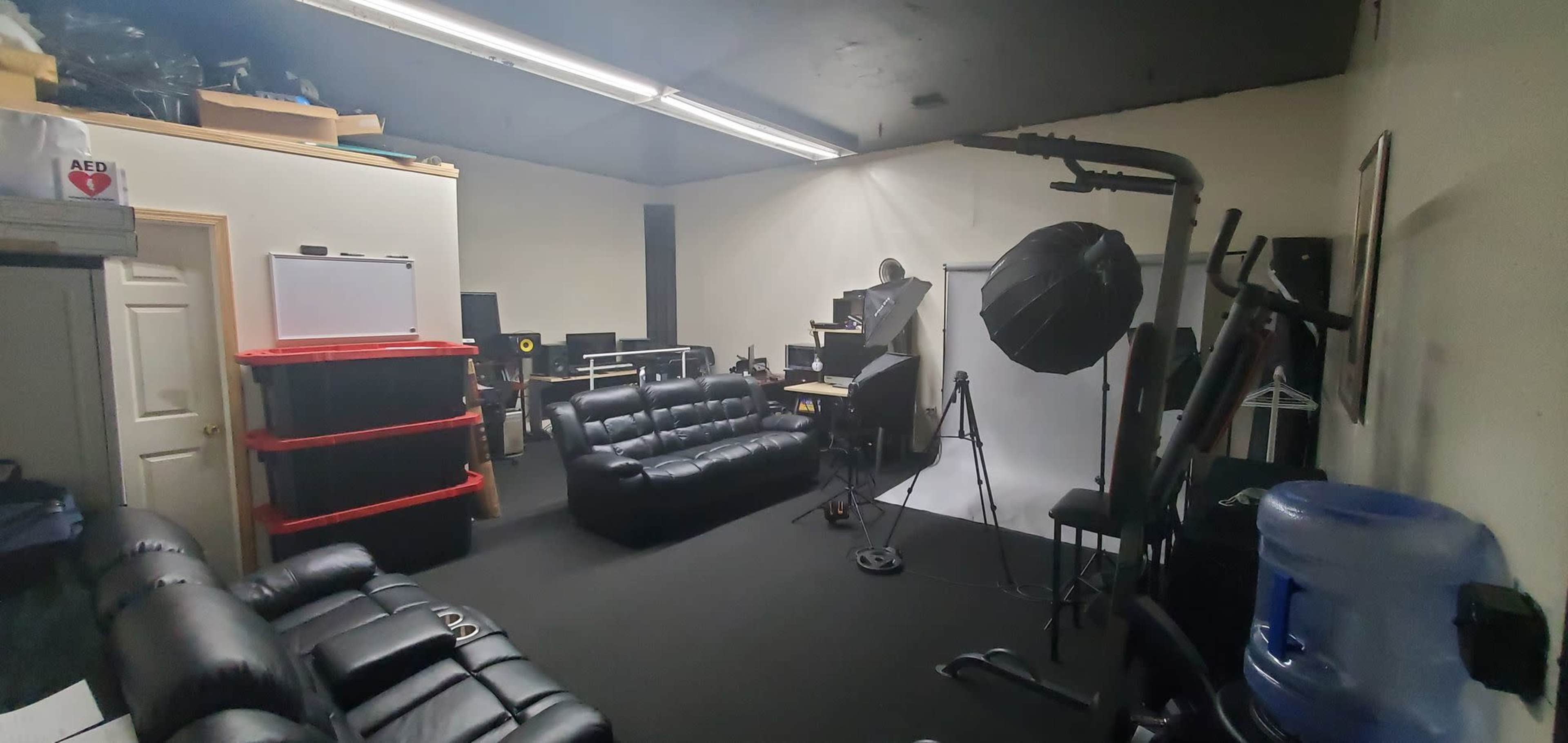 A studio room with black sofas, shelves, equipment, and a backdrop for photography or videography.