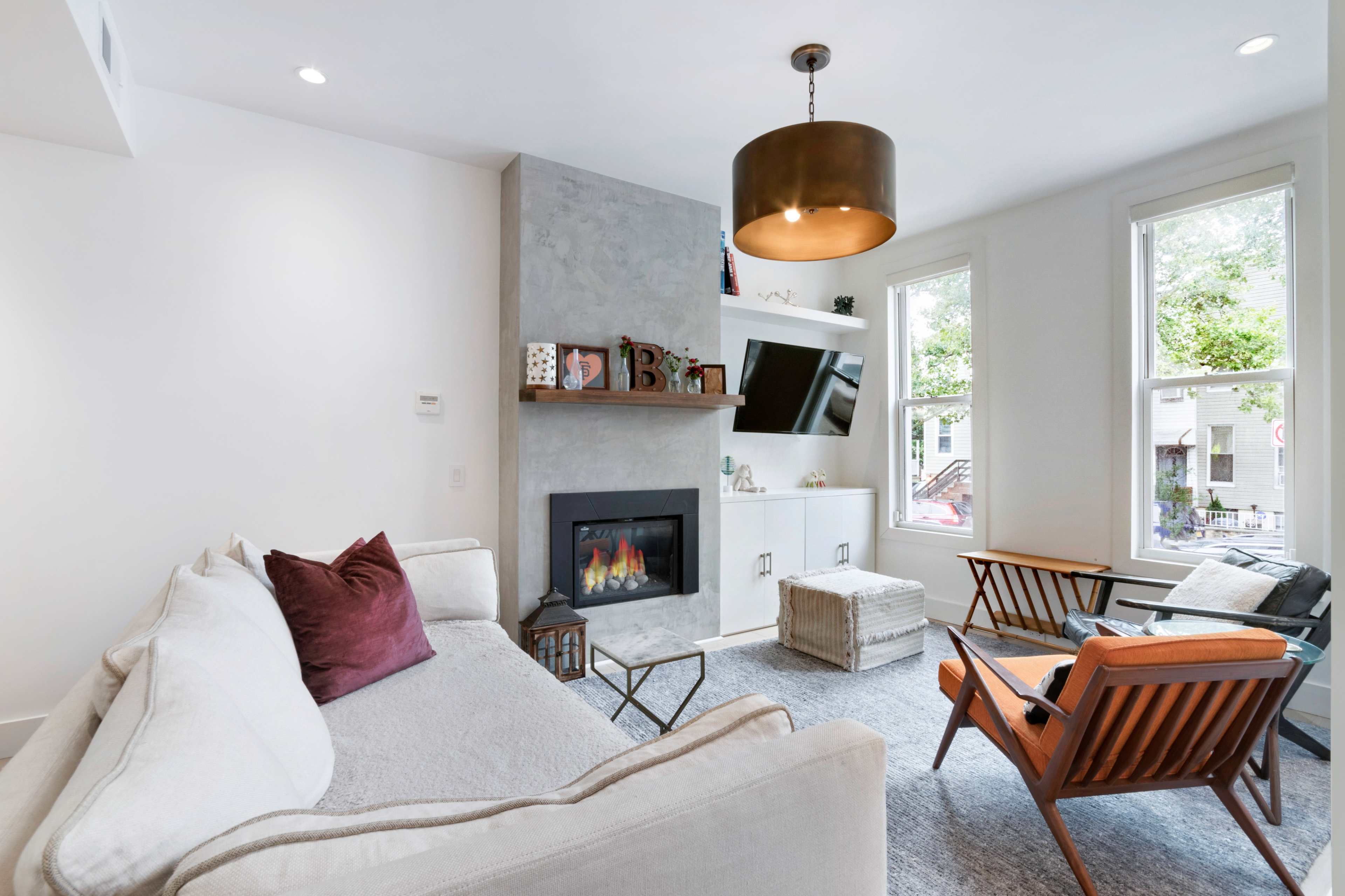 A modern living room features a cozy sofa, a gas fireplace, a mounted TV, and large windows allowing natural light.