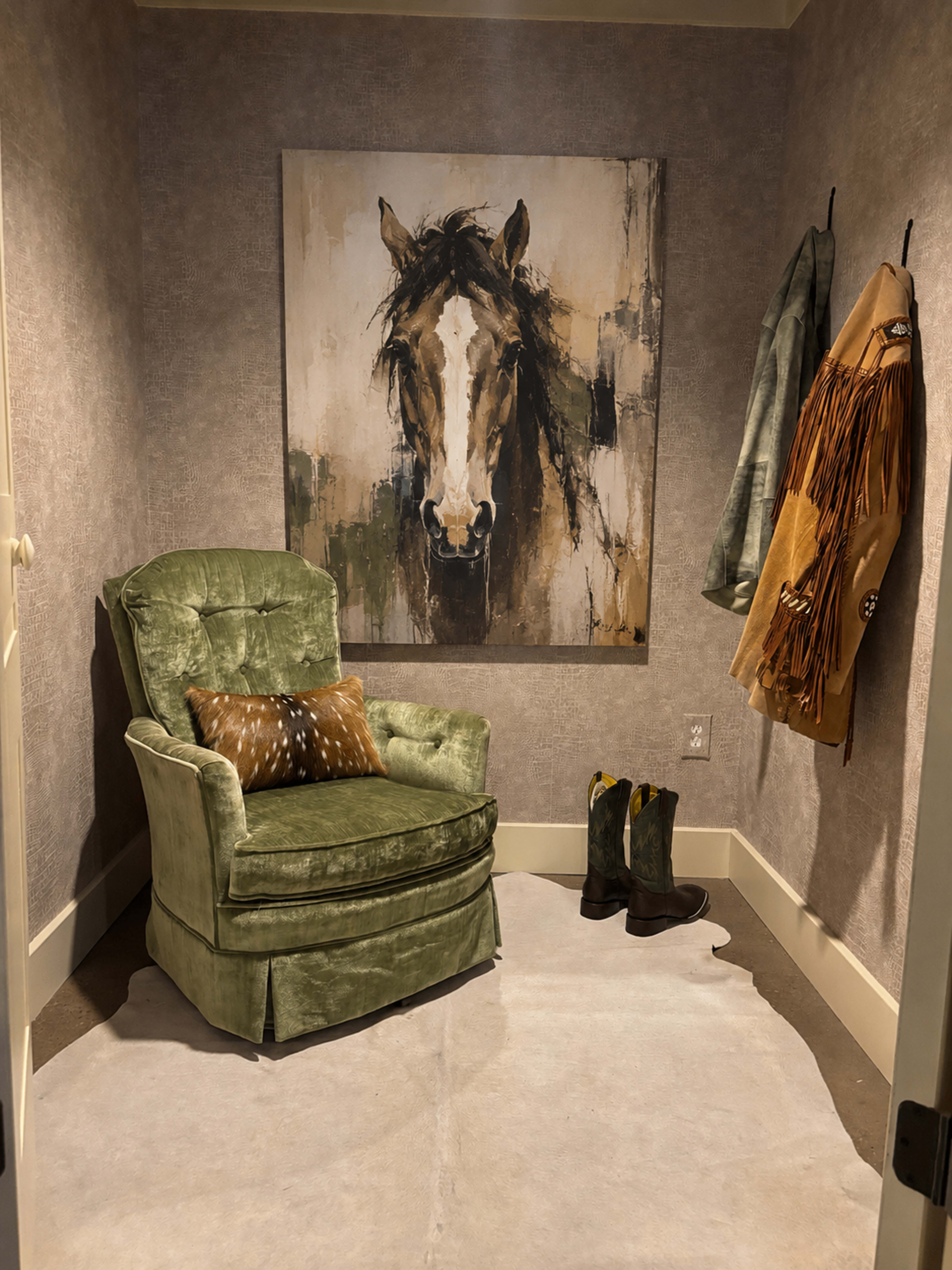 The image shows a small corner of a room featuring a green armchair, a horse painting on the wall, a fringed coat hanging, and a pair of cowboy boots on the floor.
