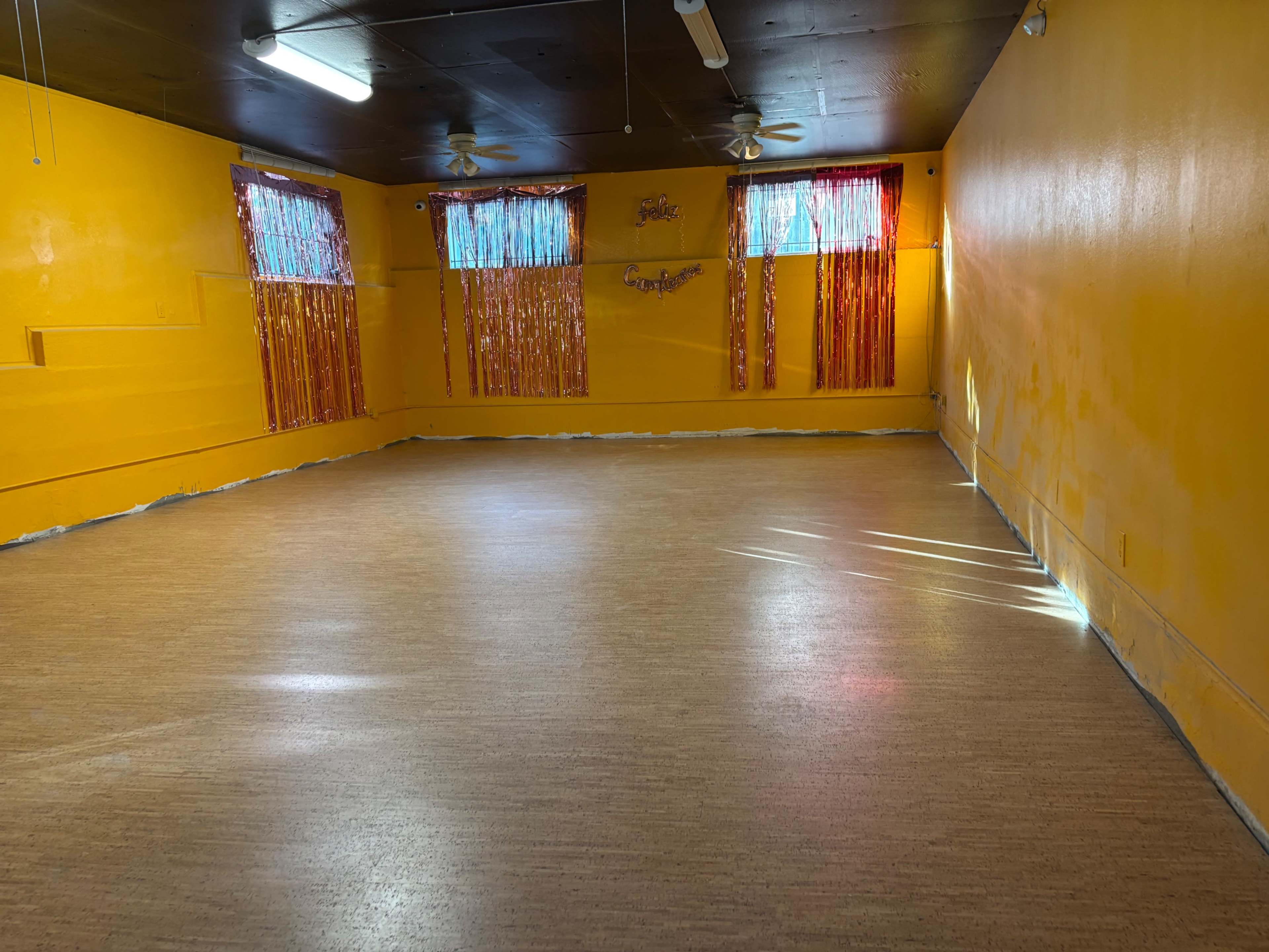 The image shows an empty room with yellow walls, light-colored flooring, and windows covered with bright, reflective curtains.
