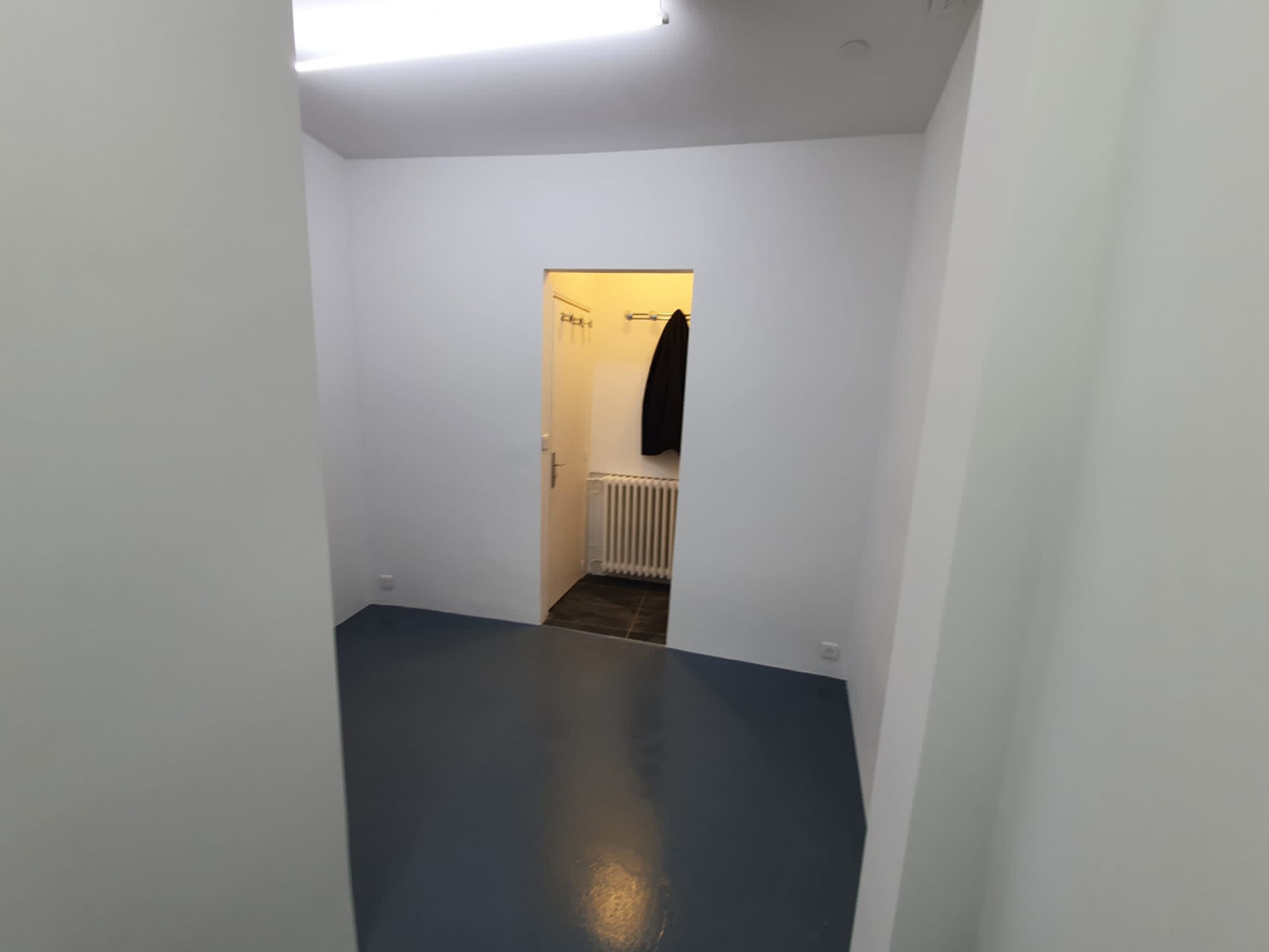 A sparsely furnished room with white walls, a door leading to another space, and a dark object hanging on a hook.
