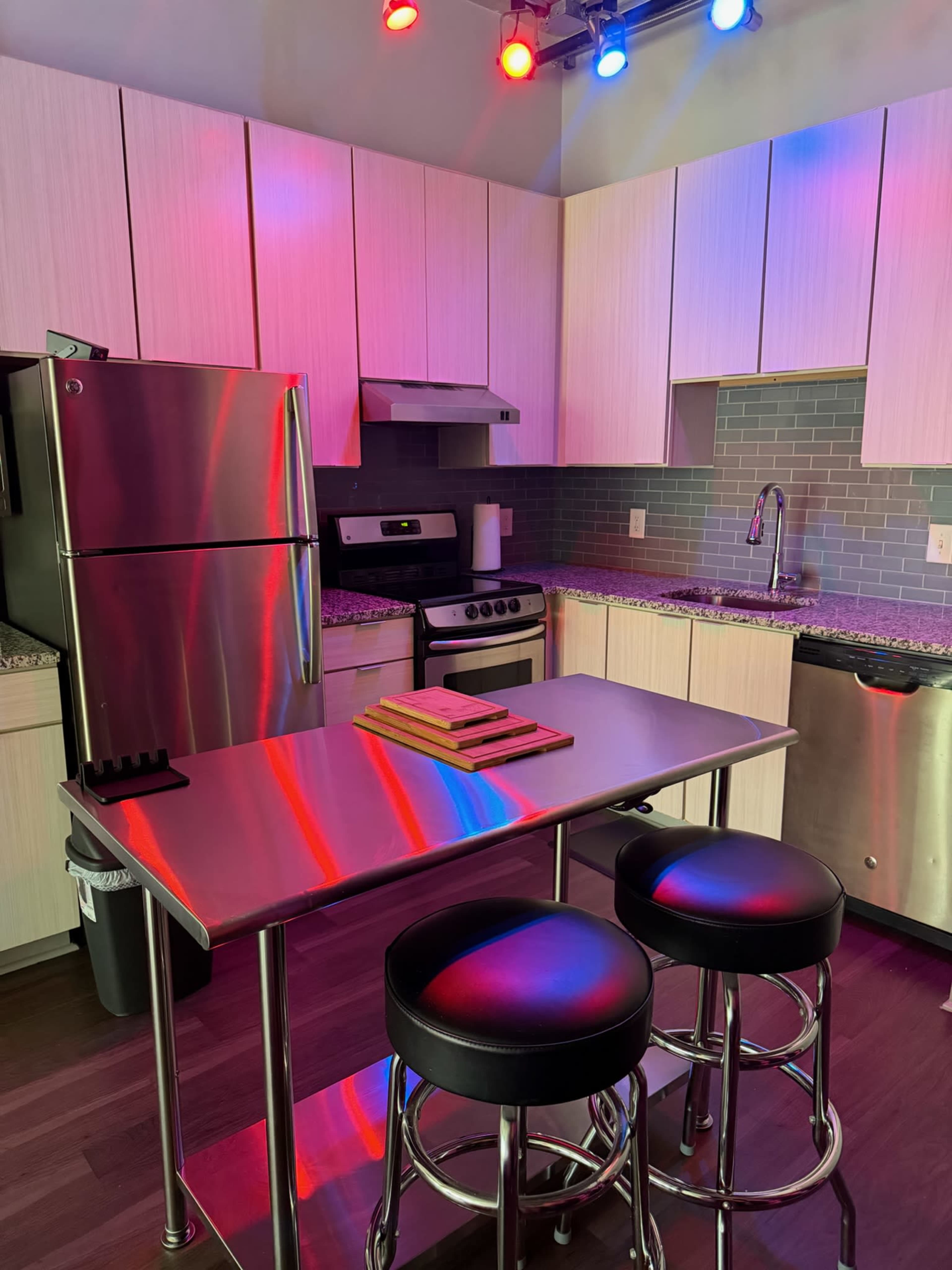 The image shows a modern kitchen with stainless steel appliances, including a refrigerator and stove, along with a central island featuring two black stools.