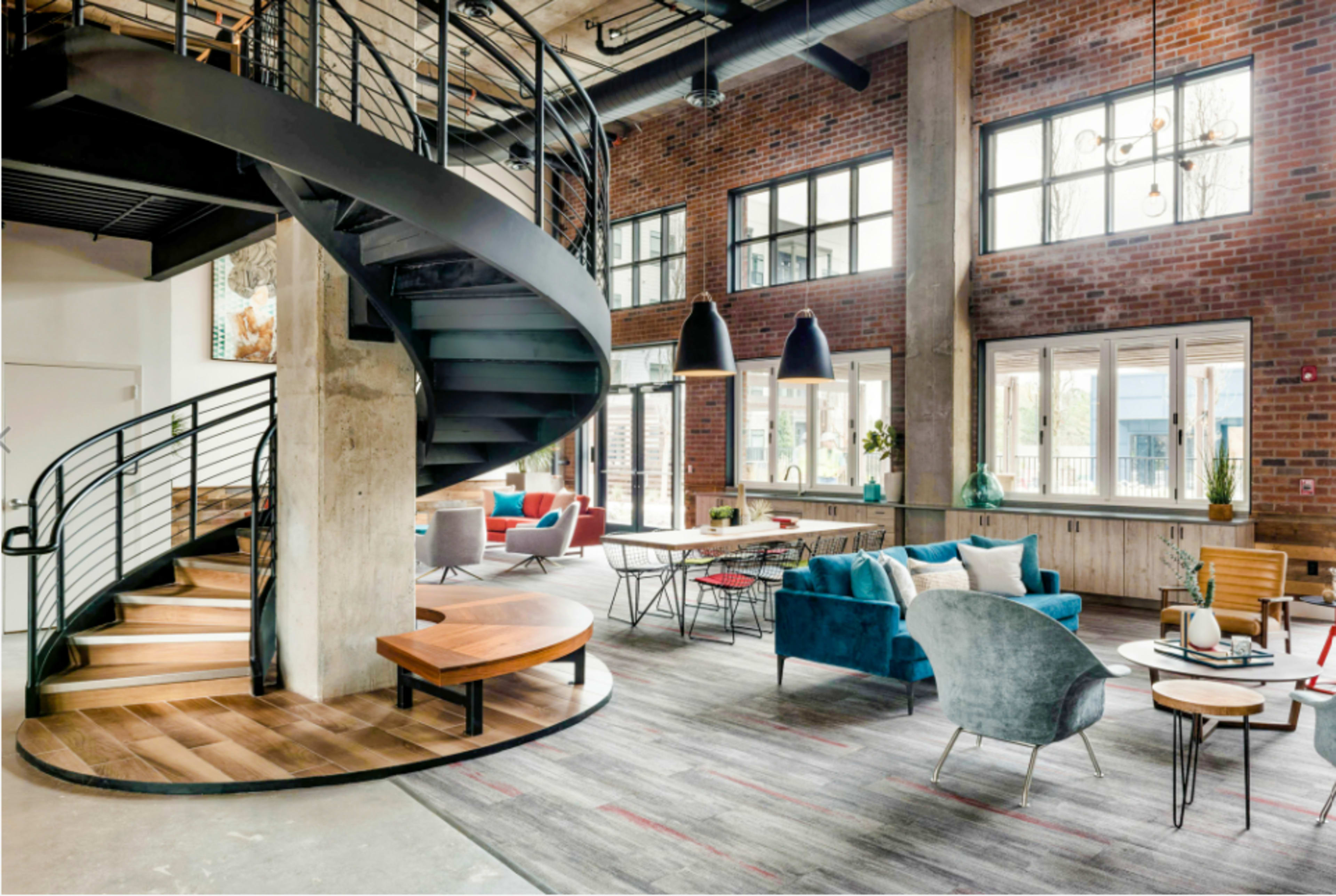 The image shows a spacious interior featuring a spiral staircase, modern furniture, and large windows allowing natural light.