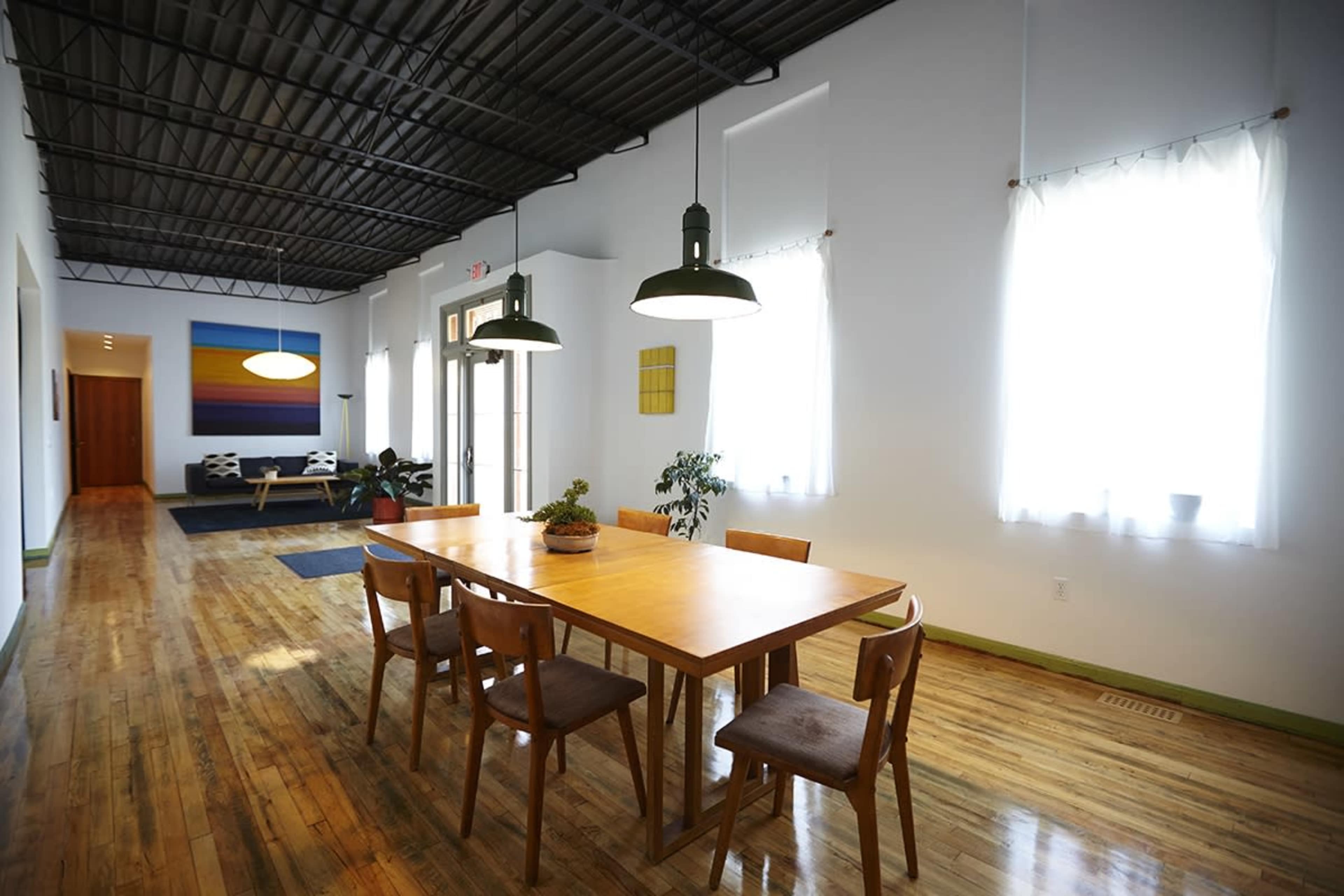 A spacious dining area features a long wooden table surrounded by chairs, with large windows allowing natural light to fill the room.