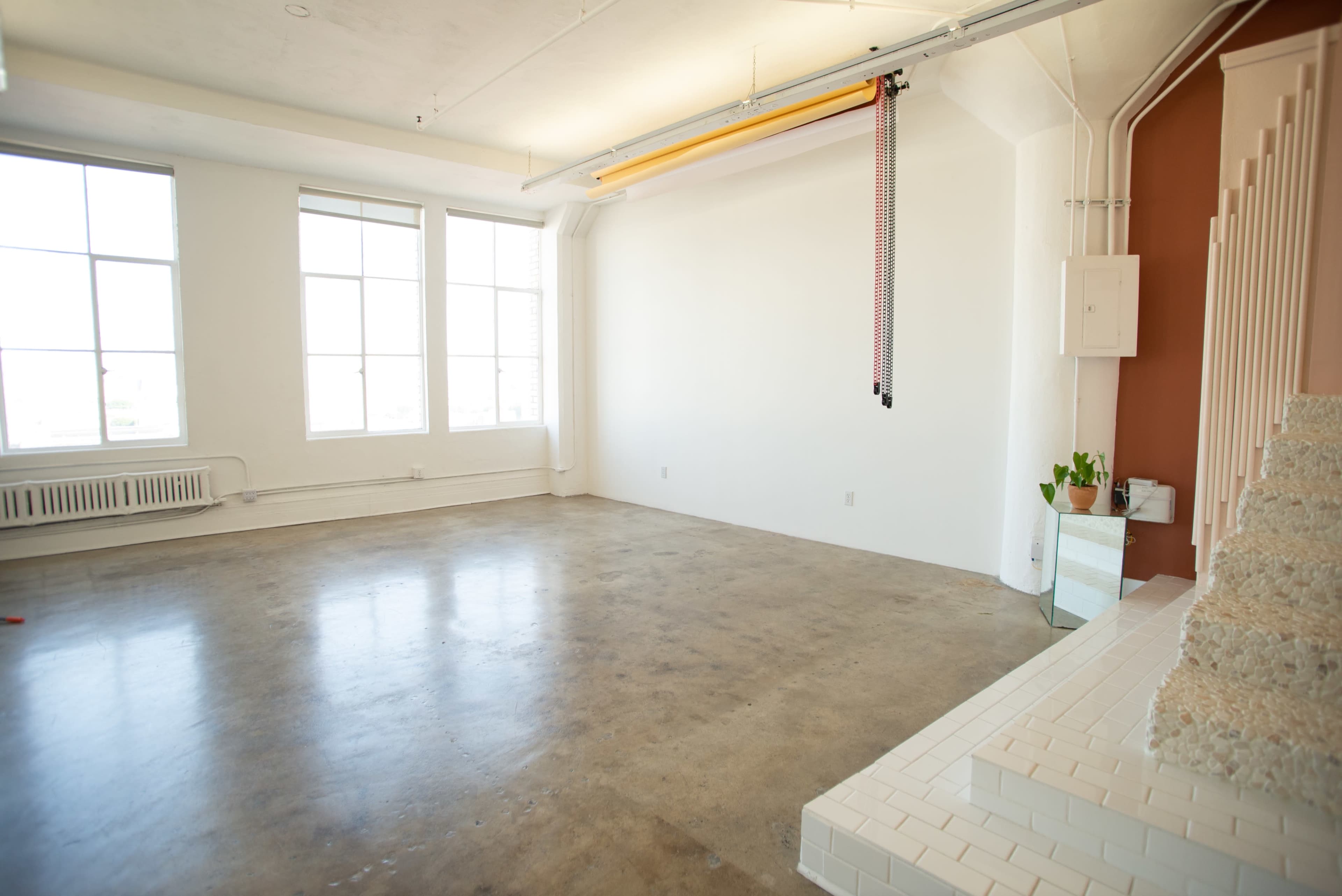 A spacious, empty room with concrete flooring, large windows, and minimal furnishings.