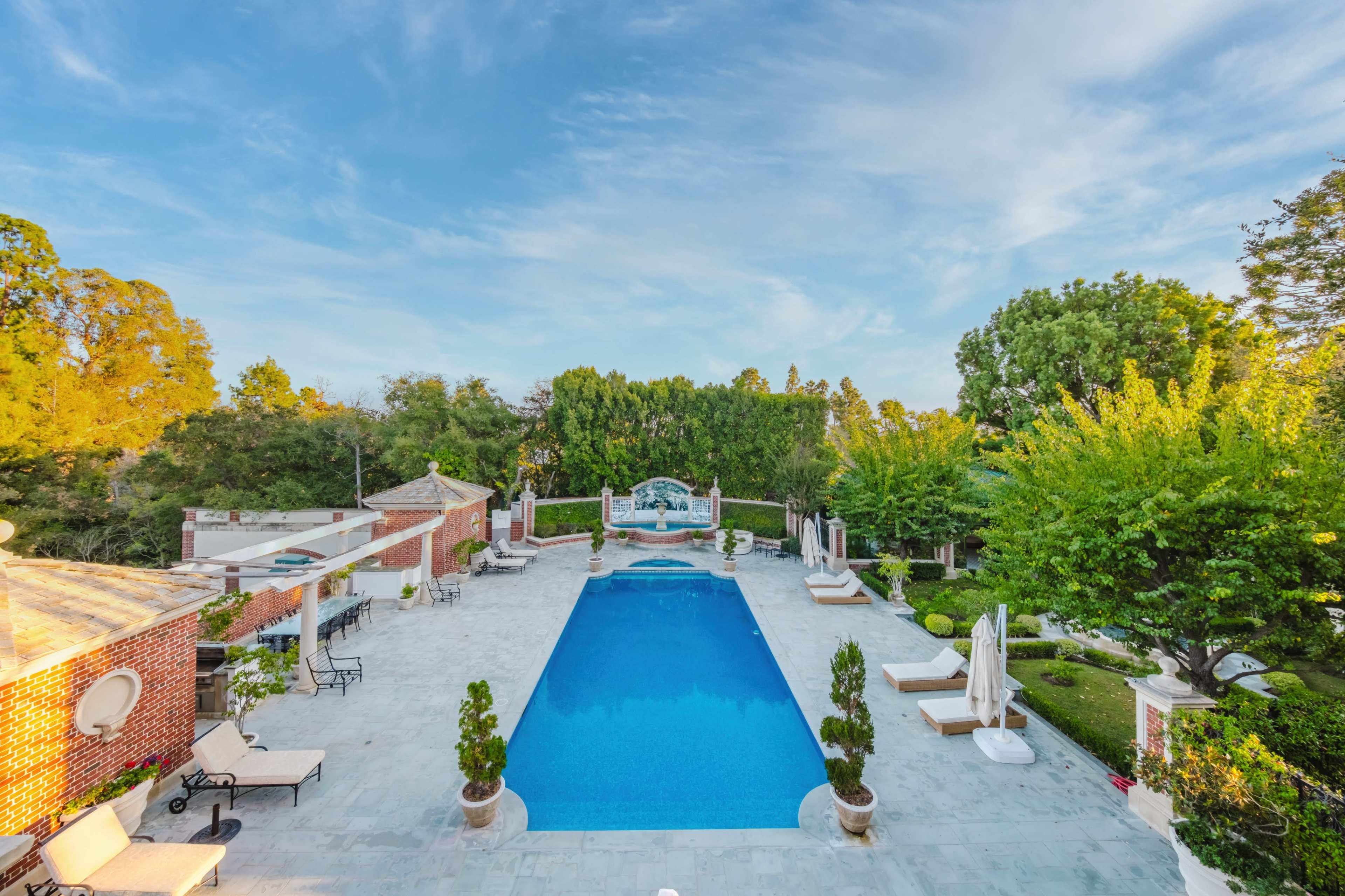 The image shows a large, rectangular swimming pool surrounded by lounge chairs and well-manicured landscaping.