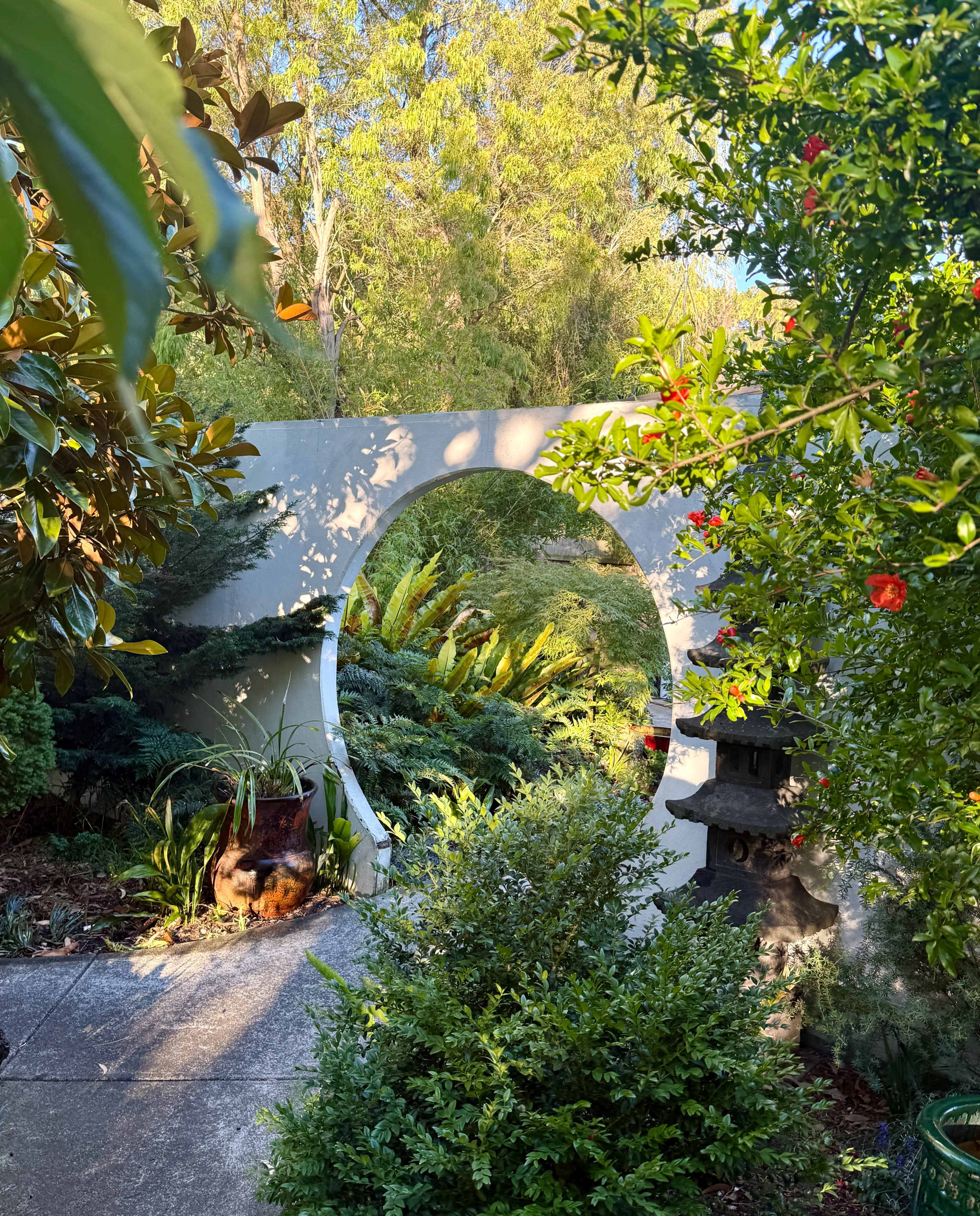 A circular stone archway frames a lush garden filled with greenery and colorful plants.