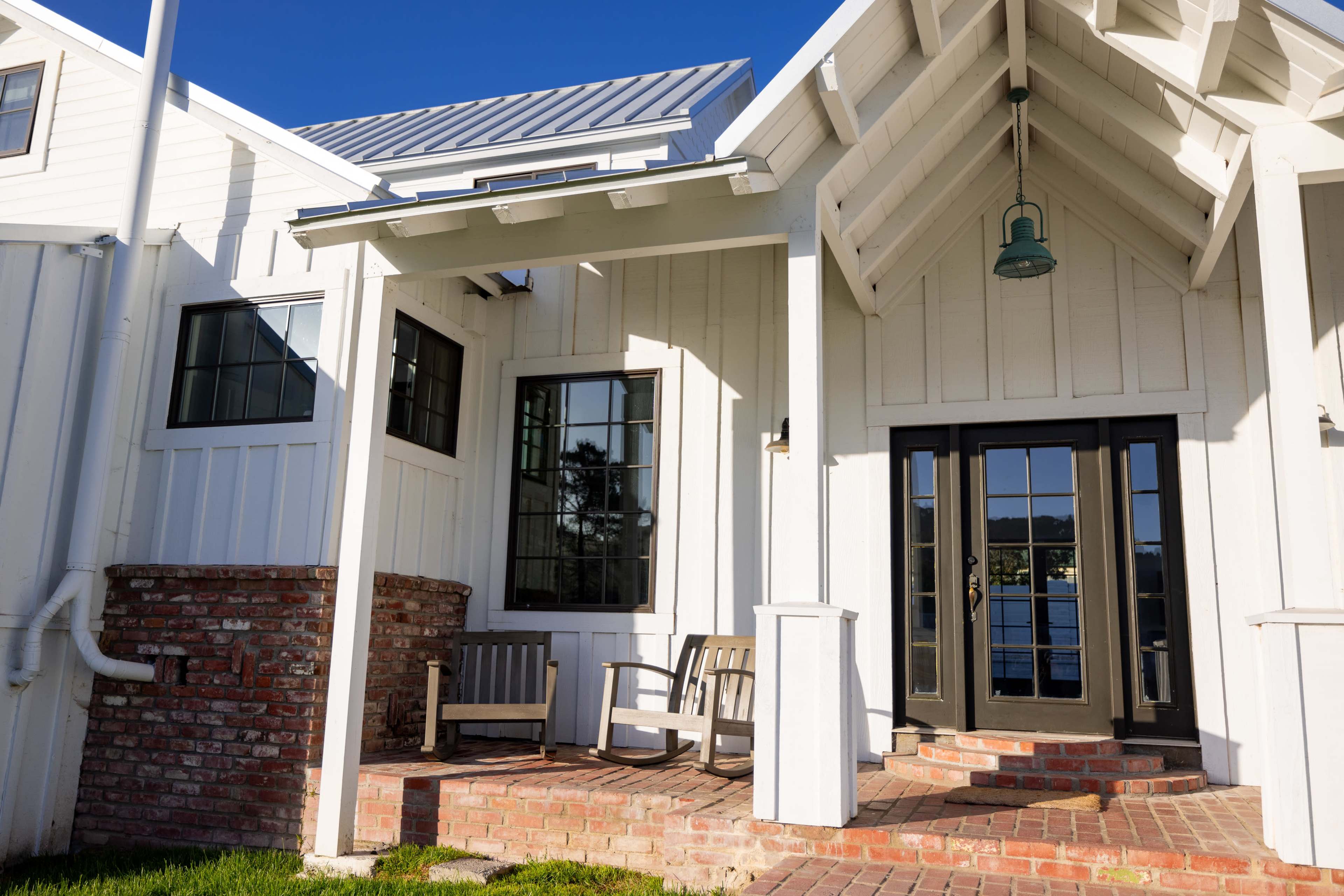 A white house with a brick porch and two wooden chairs under a triangular roof overhang.