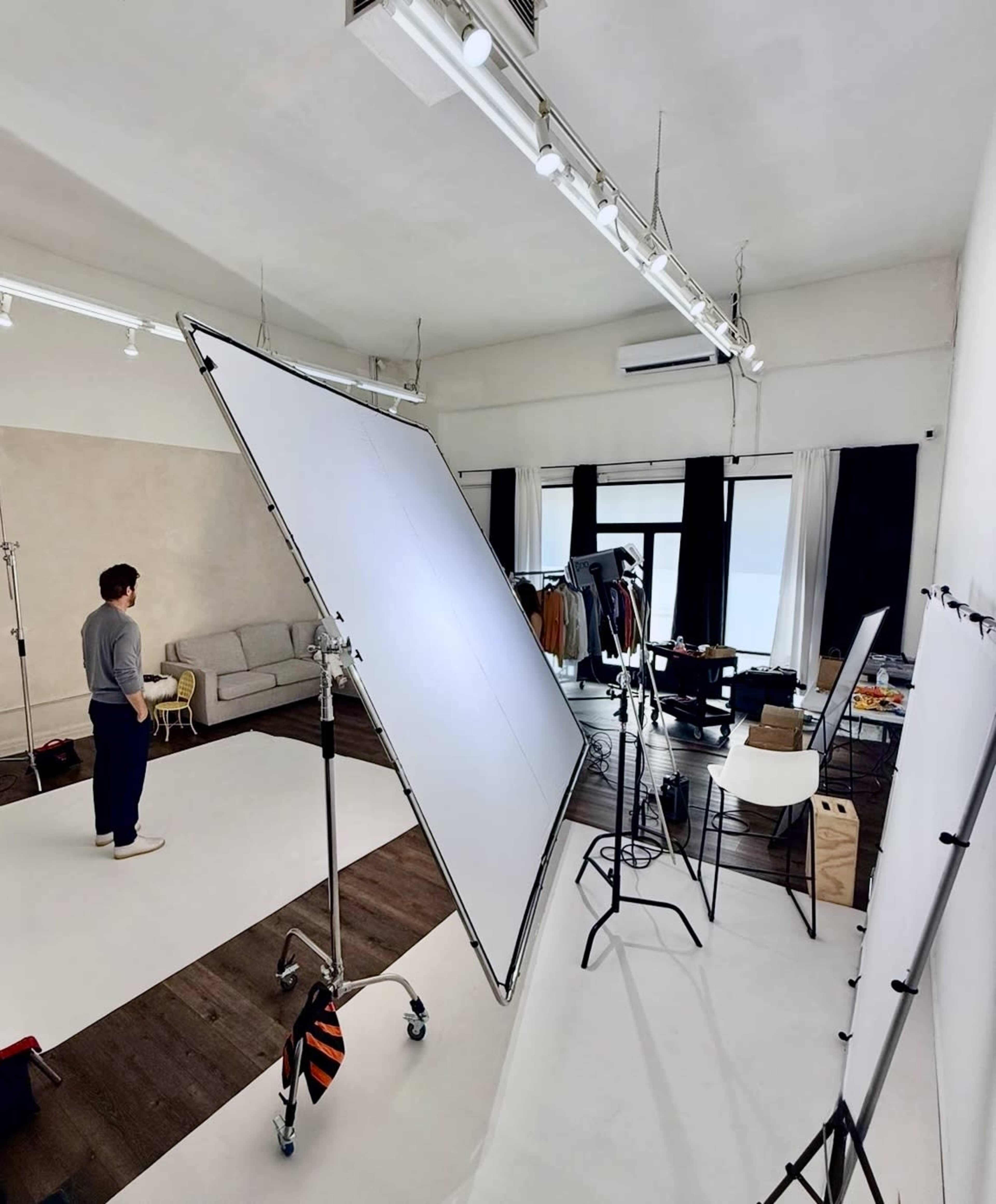 A person stands in a photography studio next to large softboxes and various pieces of clothing on display.