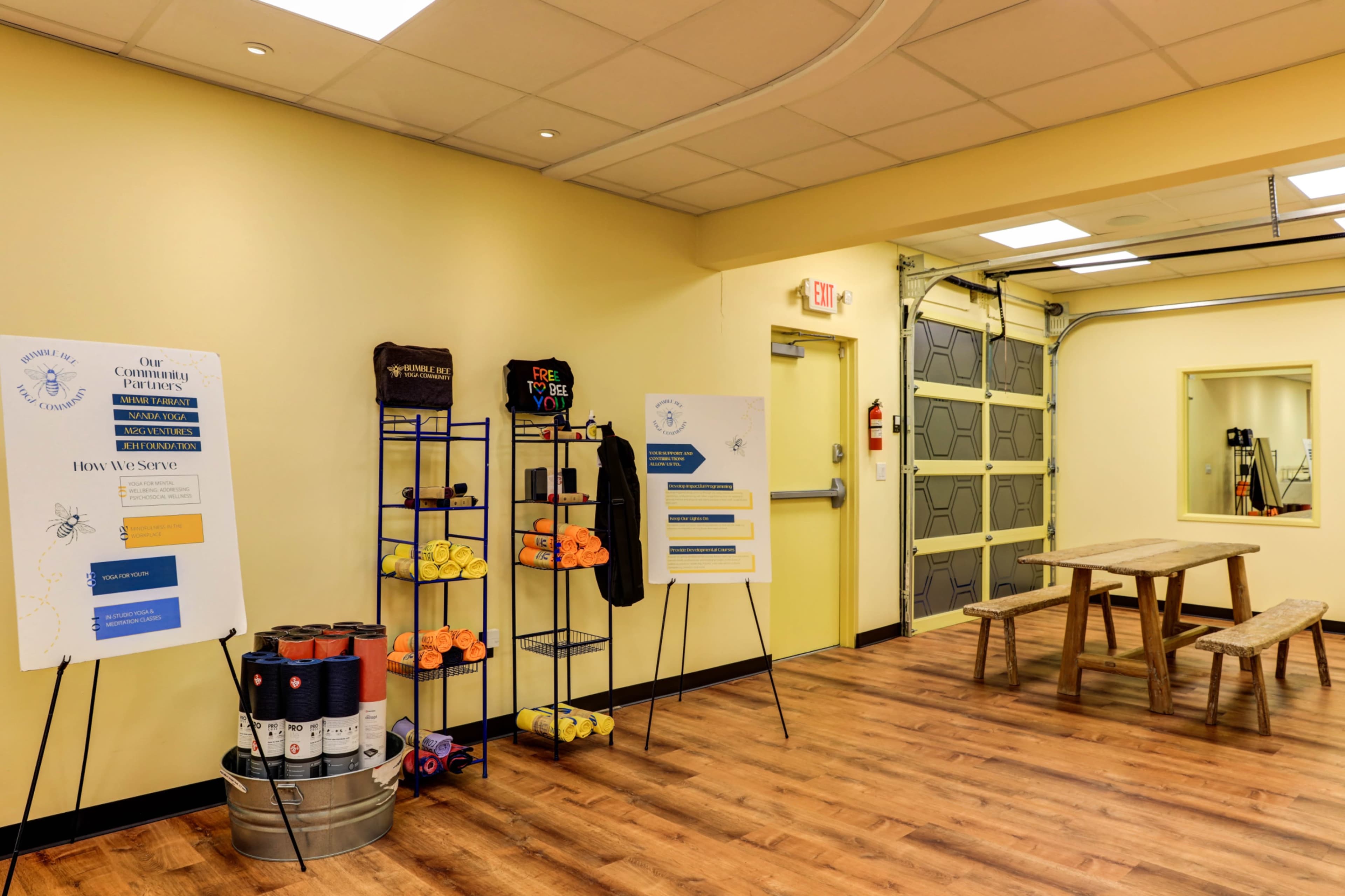 A brightly lit room featuring informational posters, exercise equipment on shelves, and a wooden picnic-style table.