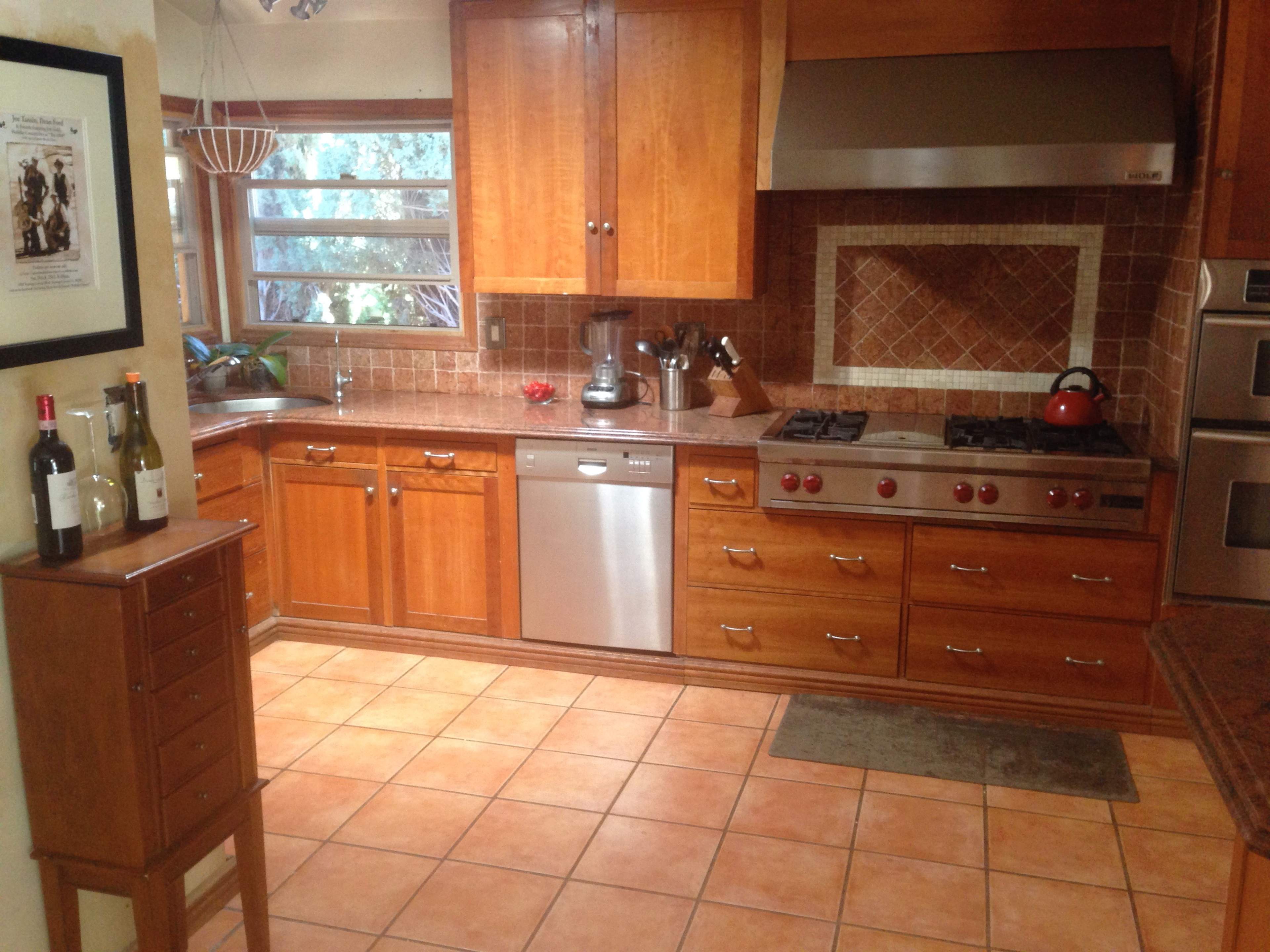 A kitchen with wooden cabinetry, a stainless steel dishwasher, a gas stove with multiple burners, and a tiled floor.
