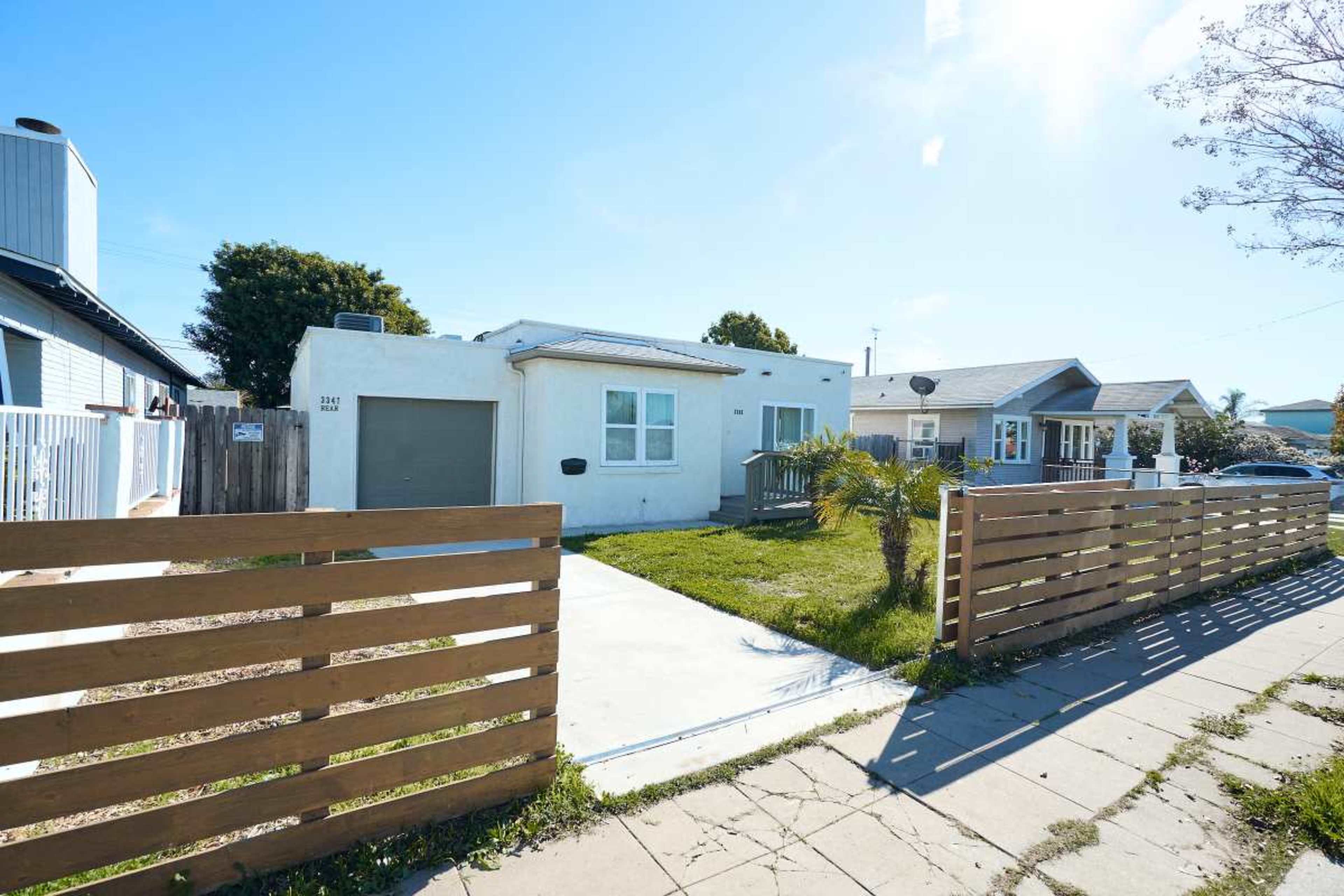 The image shows a single-story house with a front yard, bordered by a wooden fence and driveway leading to a garage.
