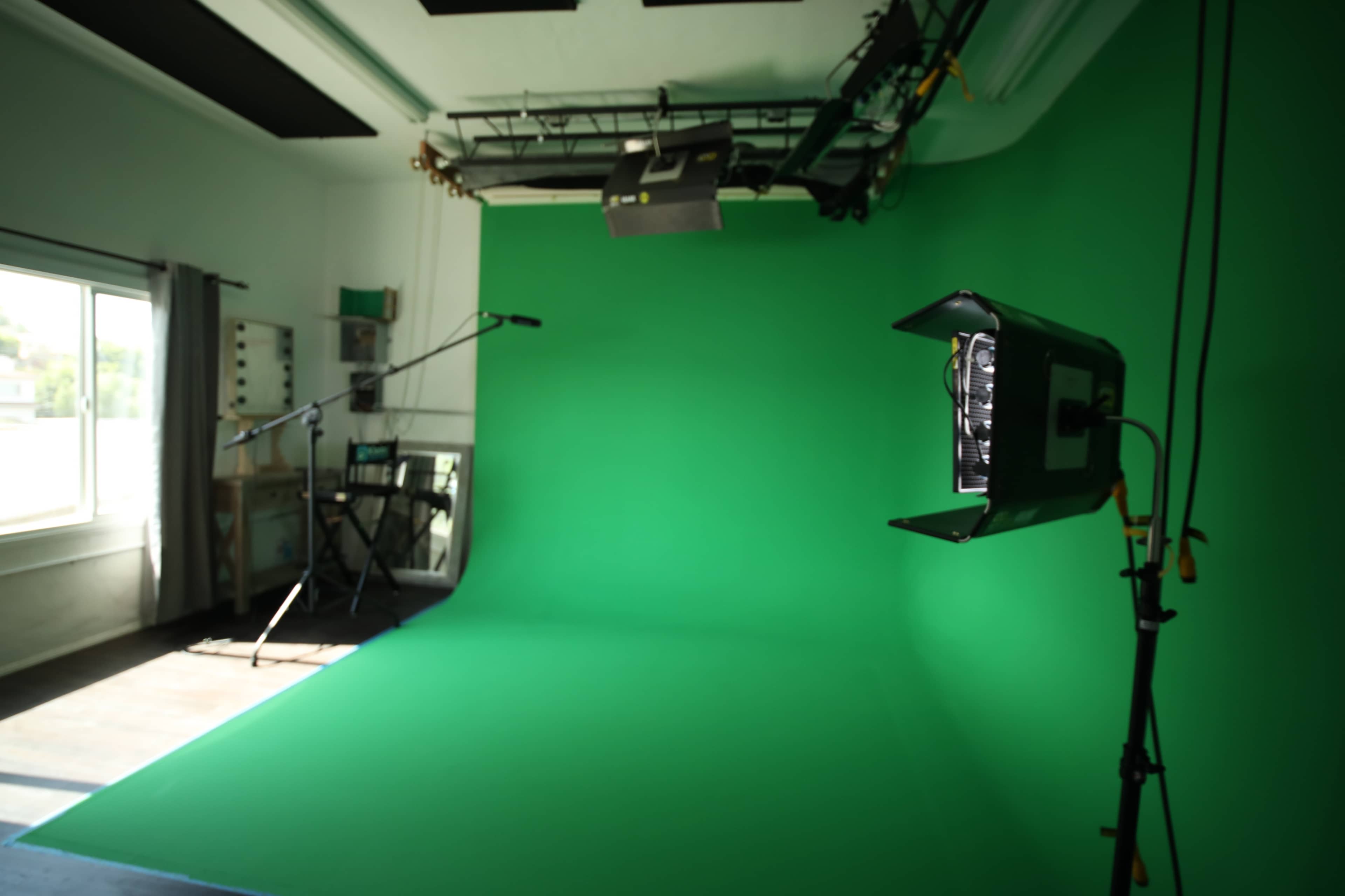 A photography studio with a green screen backdrop, lighting equipment, and a microphone setup.