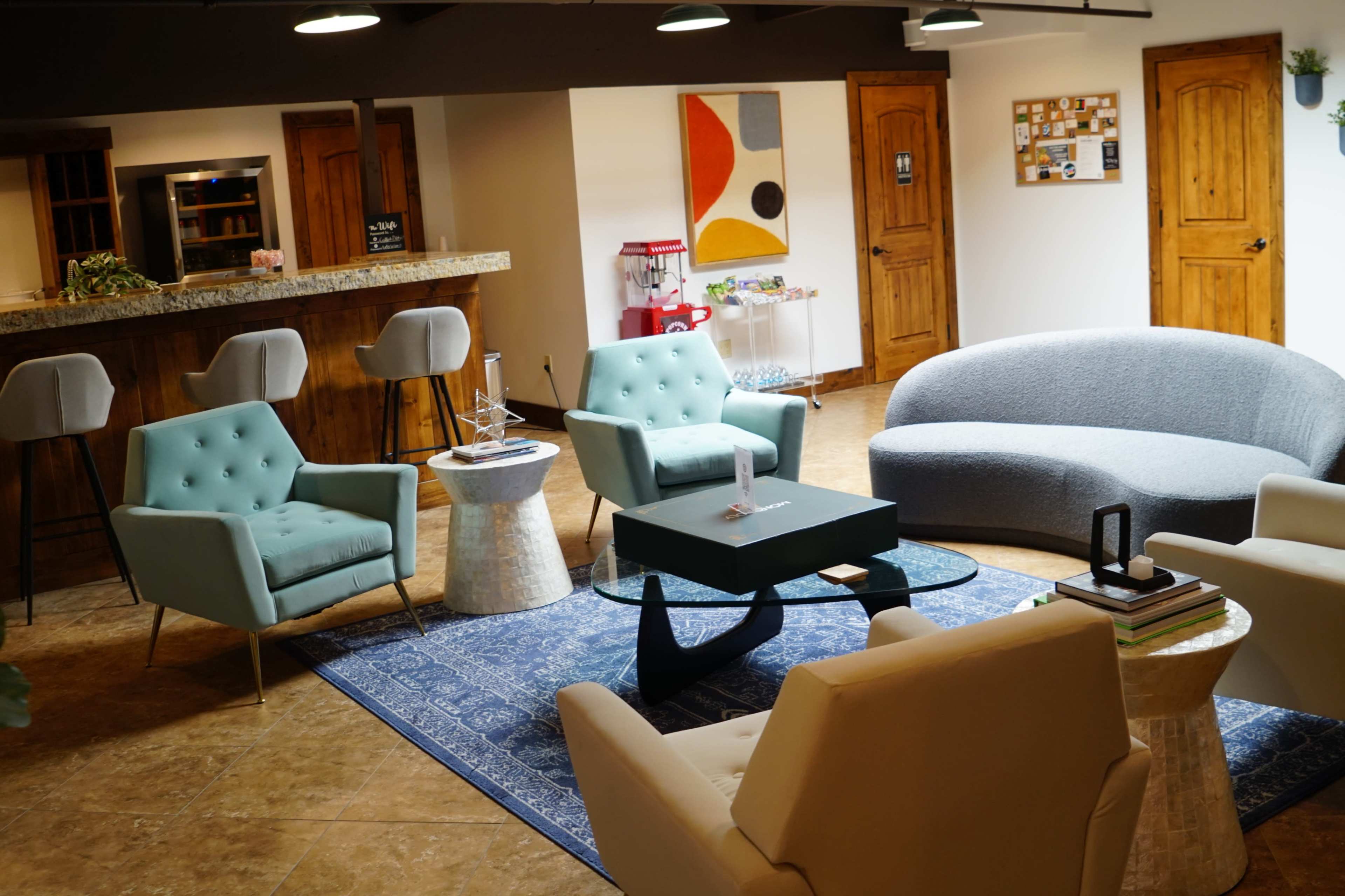 A modern lounge area furnished with several stylish chairs, a curved sofa, a glass coffee table, and a bar area in the background.