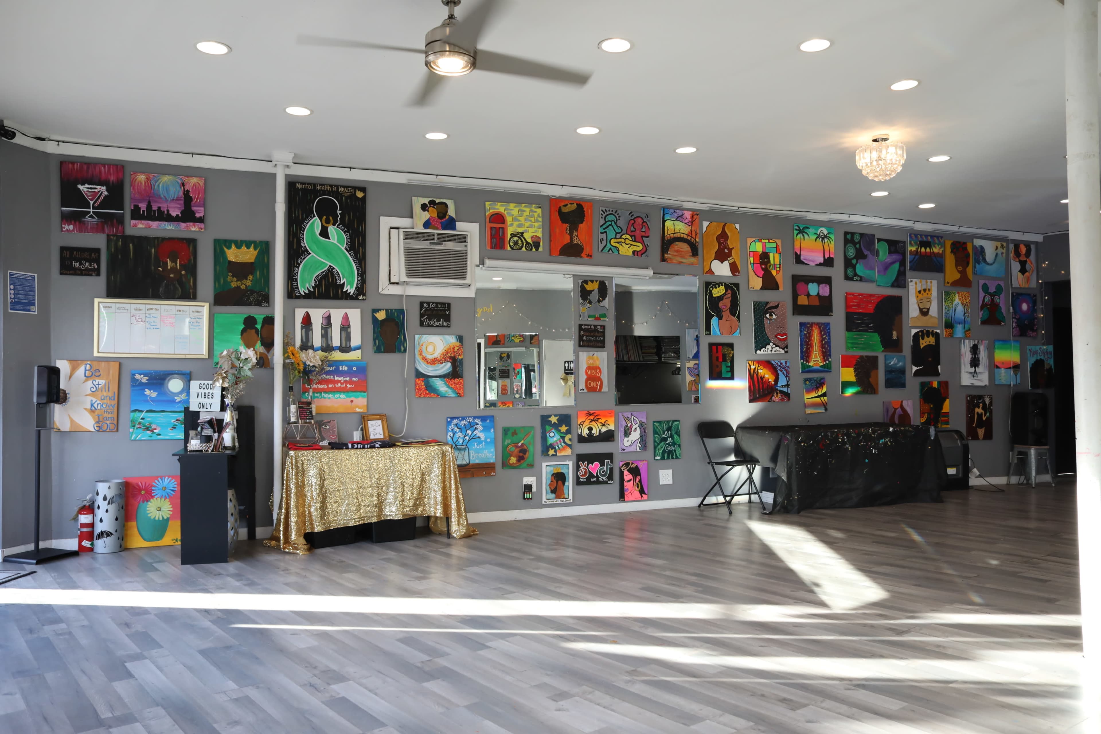 A spacious art studio with colorful paintings displayed on the walls and a small stage area with a table and chairs.