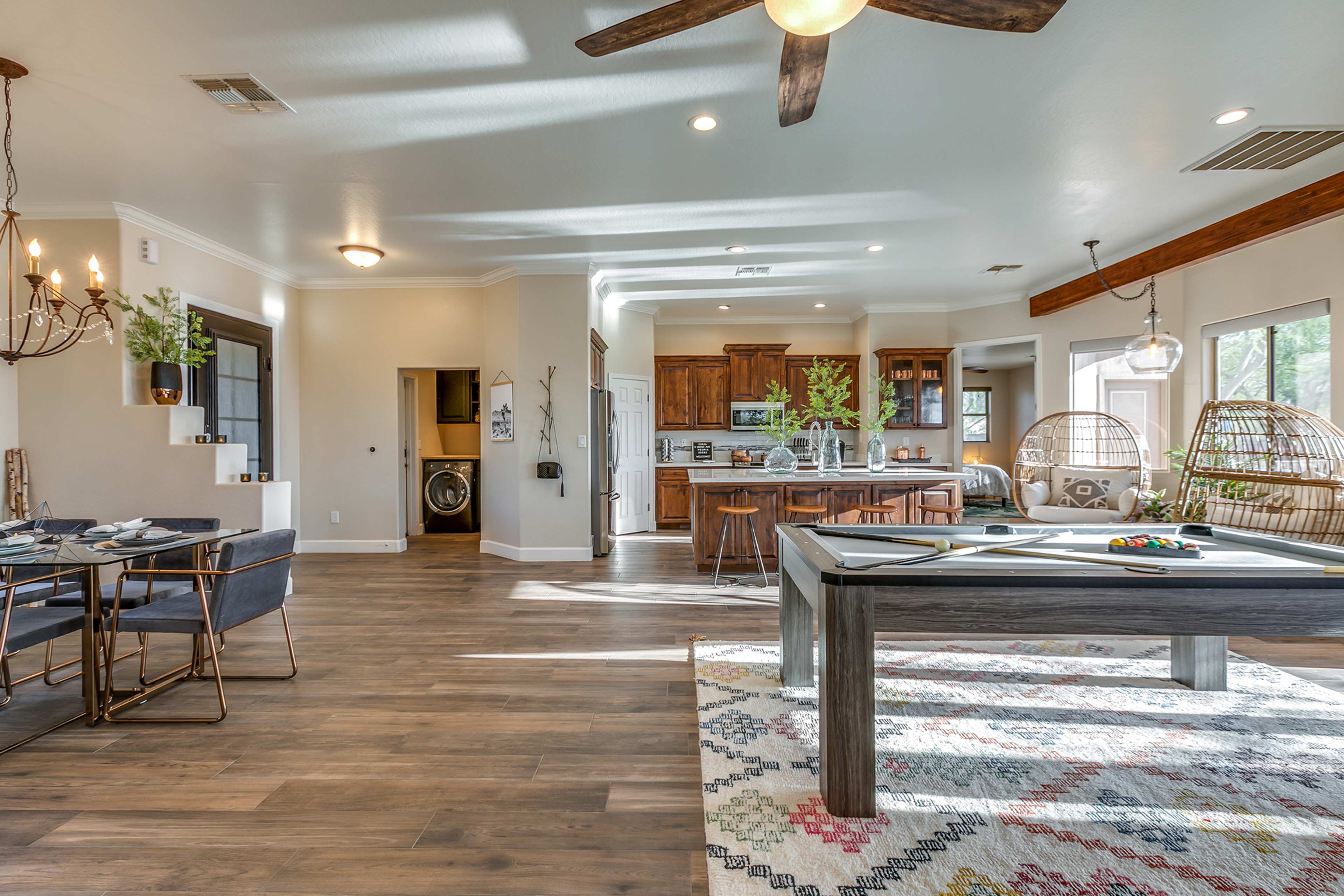 The image shows a spacious, open-plan room featuring a dining area, a kitchen with wooden cabinetry, and a billiards table in a well-lit setting.