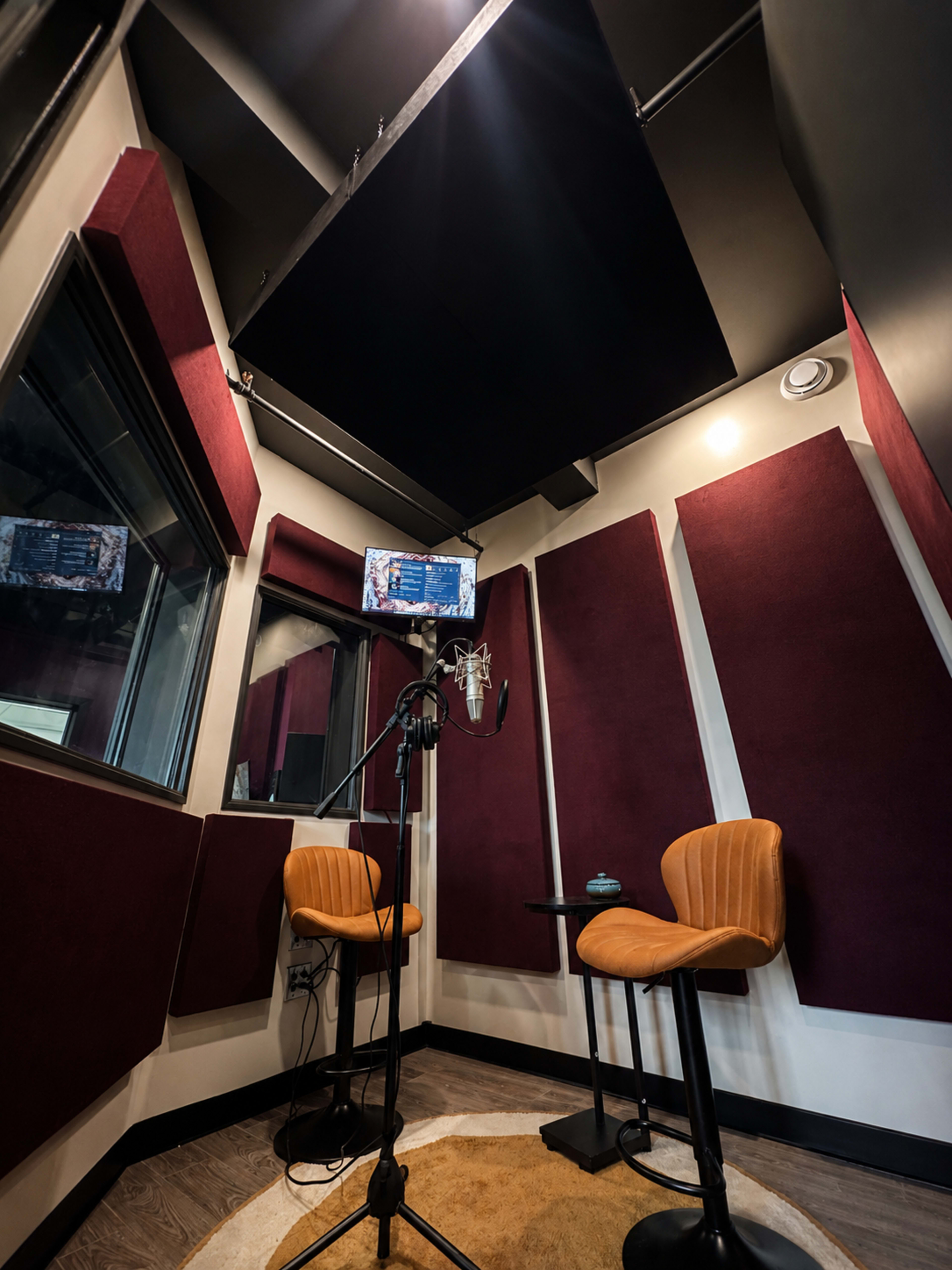 The image shows a soundproof recording booth featuring two chairs, a microphone on a stand, and acoustic panels lining the walls.
