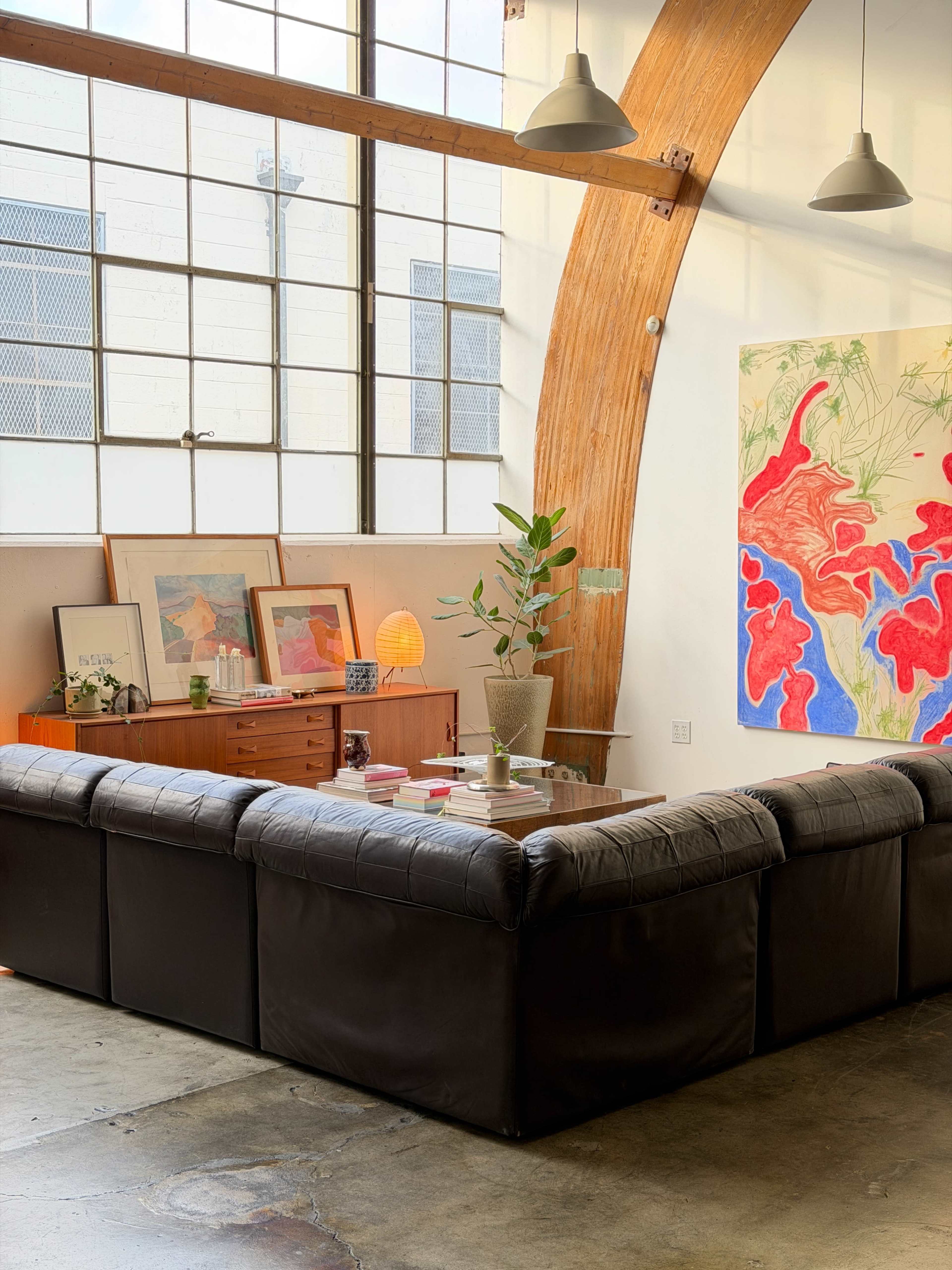 The image features a modern living space with a large black sectional sofa, an art-filled wall, and ample natural light streaming through large windows.