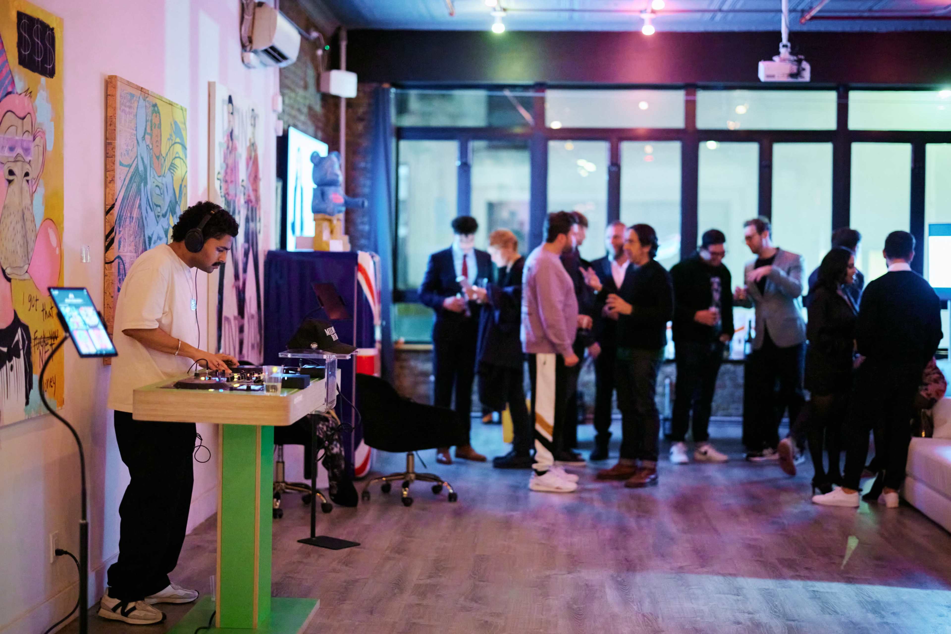 A DJ is mixing music at a vibrant event space while guests mingle and socialize in the background.