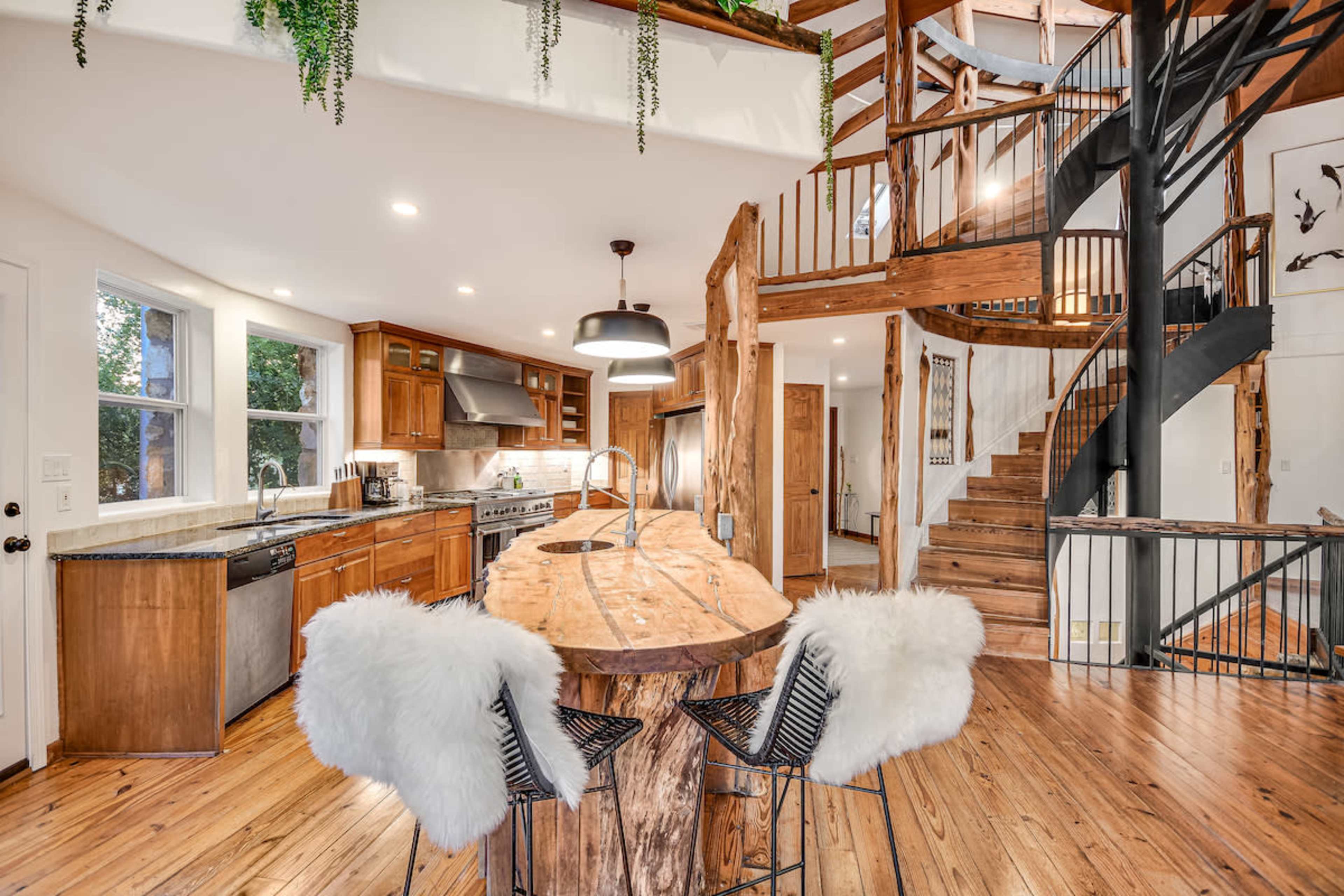 A modern kitchen with a large wooden island, black bar stools, and a spiral staircase leading to an upper floor.