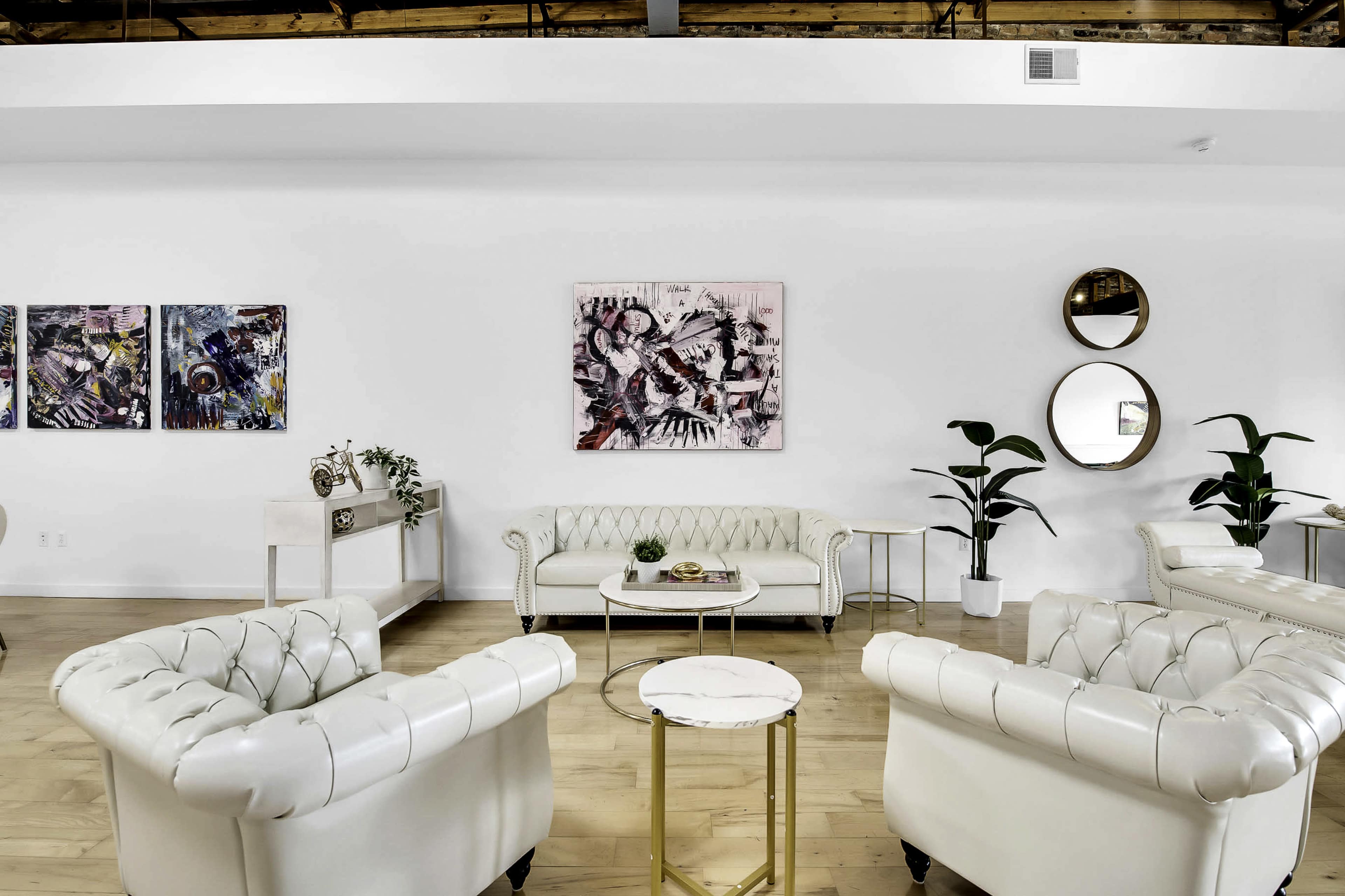 A modern, minimally decorated lounge area featuring white tufted sofas, a circular coffee table, wall art, and large mirrors.