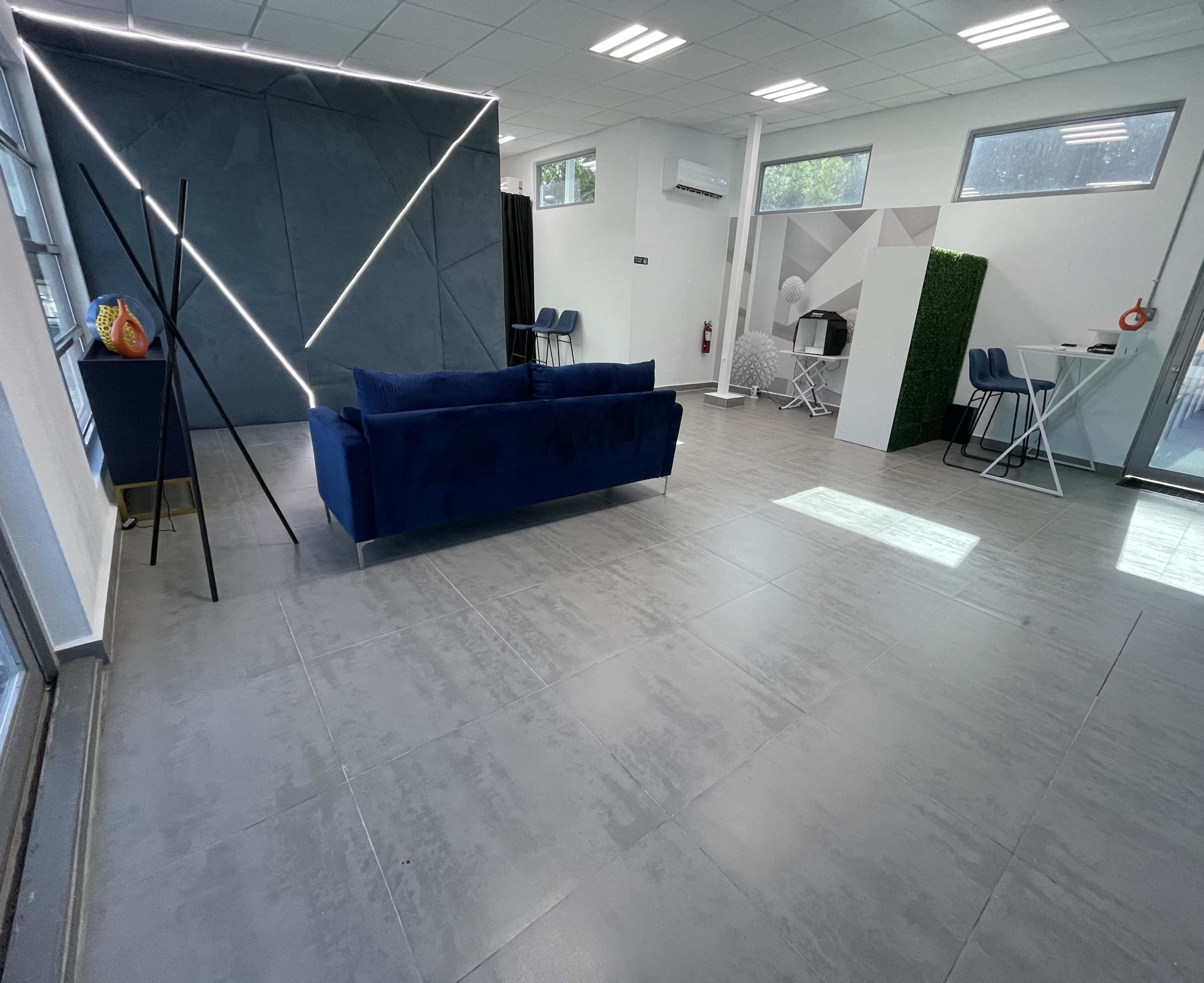 The image shows a modern, spacious interior with a blue sofa, a geometric feature wall, and minimal furniture placement.