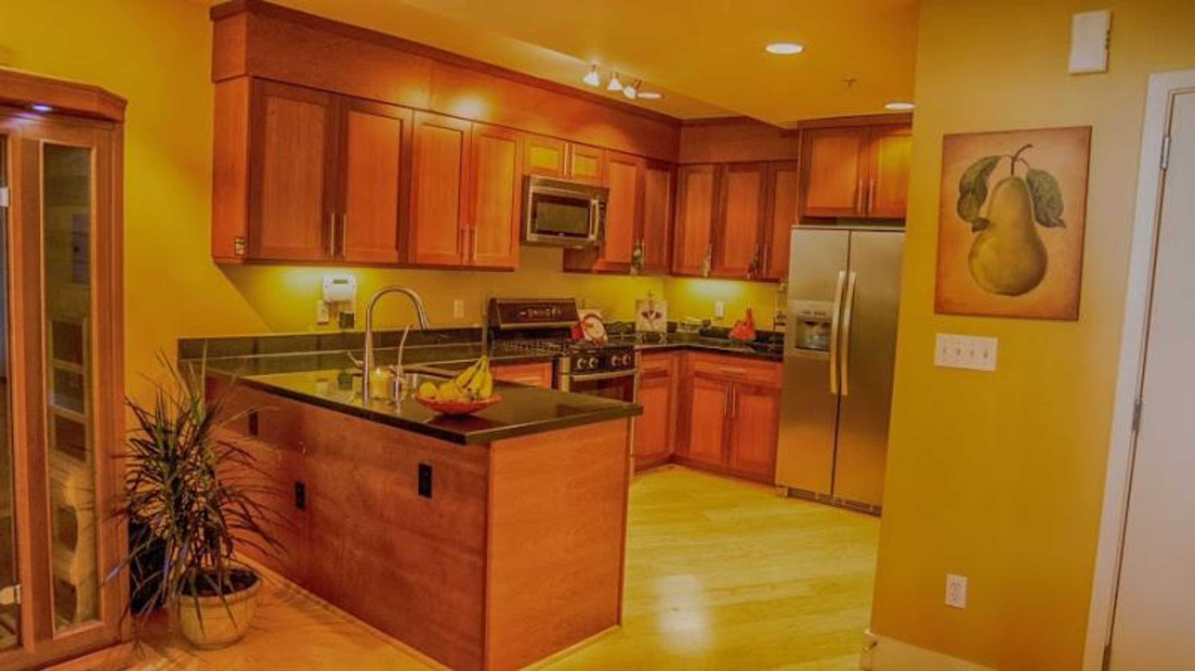 A kitchen featuring wooden cabinets, stainless steel appliances, and a centrally placed island with a bowl of fruit.