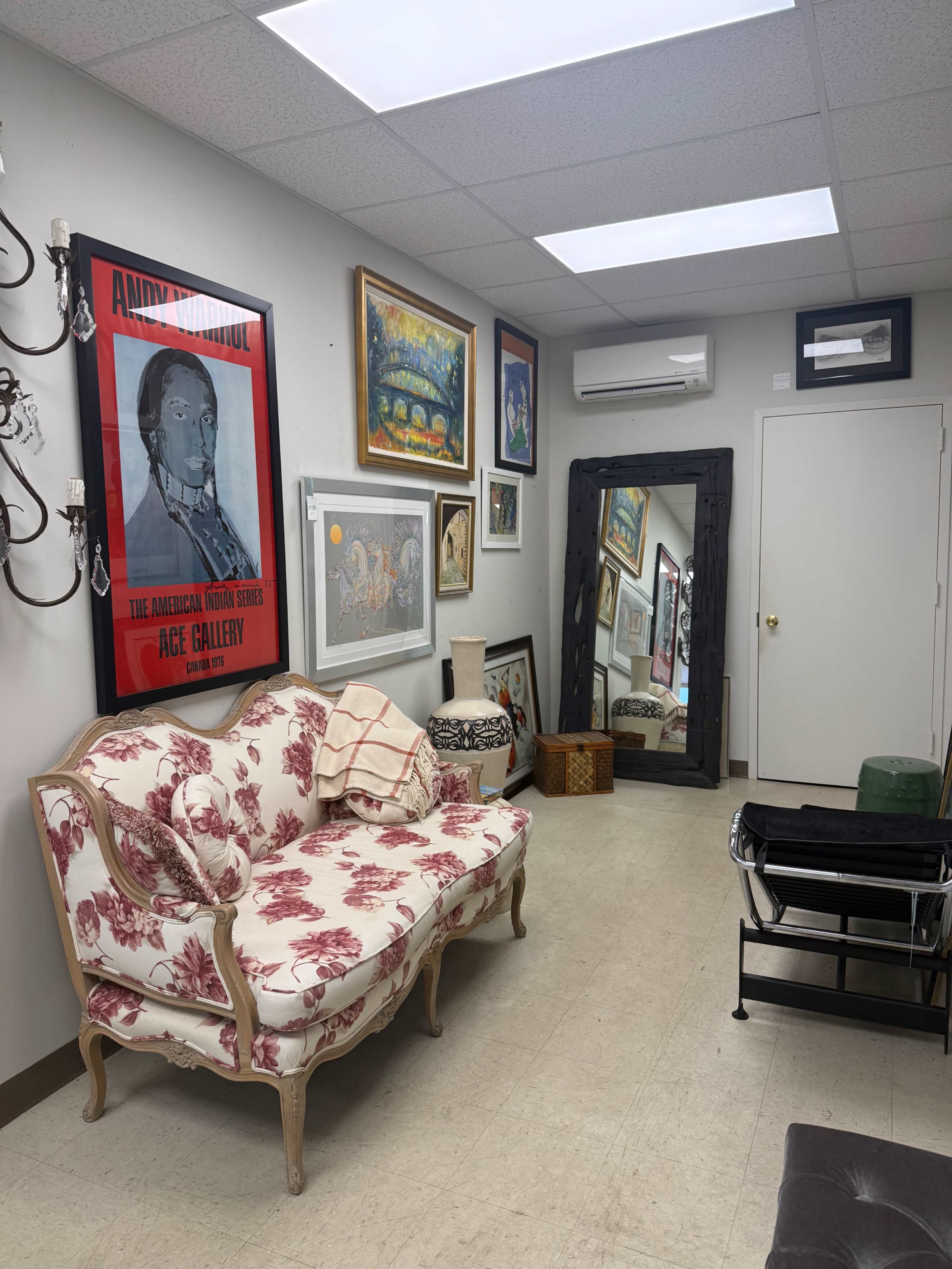The image shows a well-decorated room featuring a floral-patterned sofa, various framed artworks on the walls, and a large mirror.